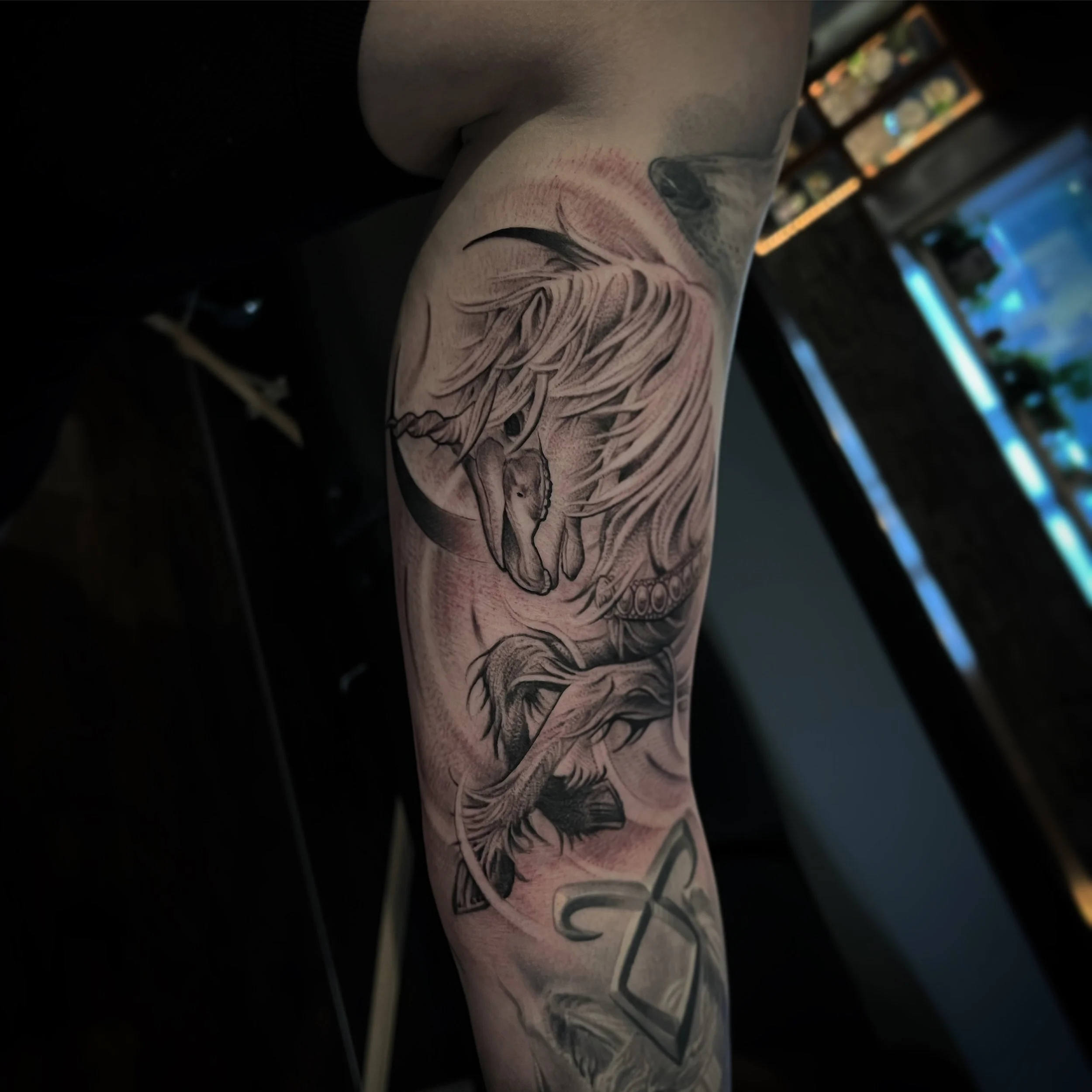 Black and gray tattoo of a horse's head and a wolf's head on an arm.