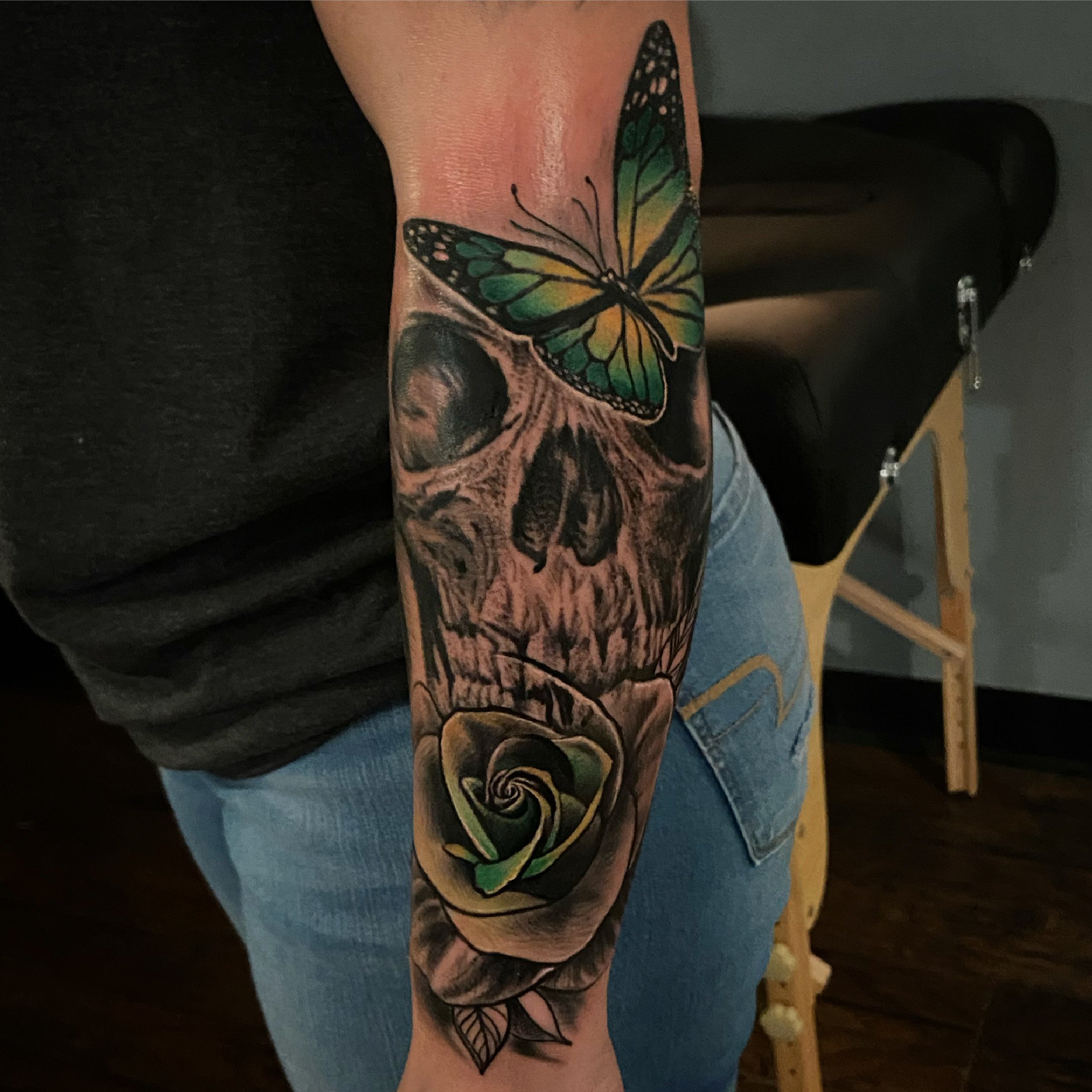 Tattoo of a butterfly, skull, and rose on a person's forearm.