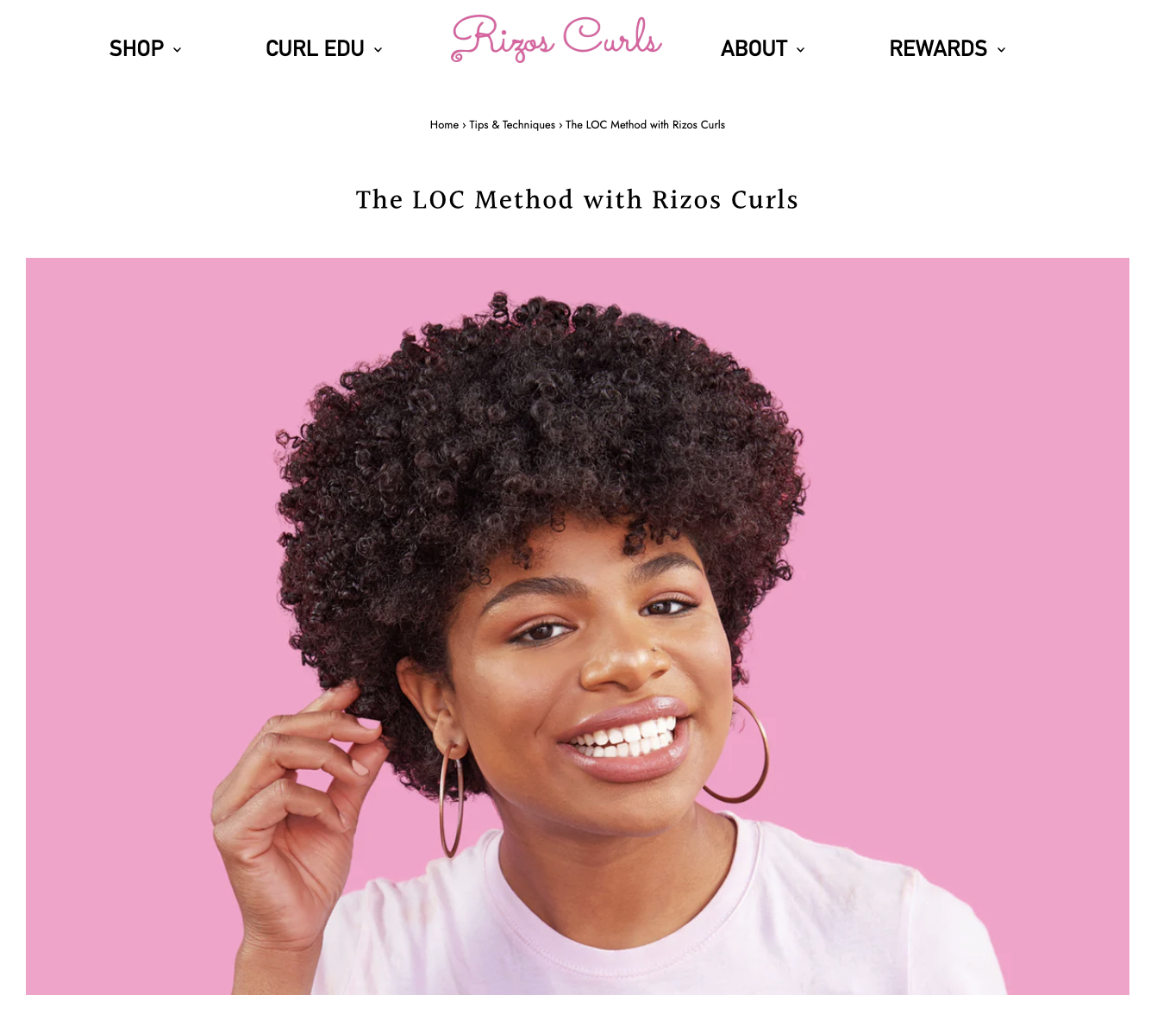 Portrait of woman smiling, curly black hair, hoop earrings, pink background.