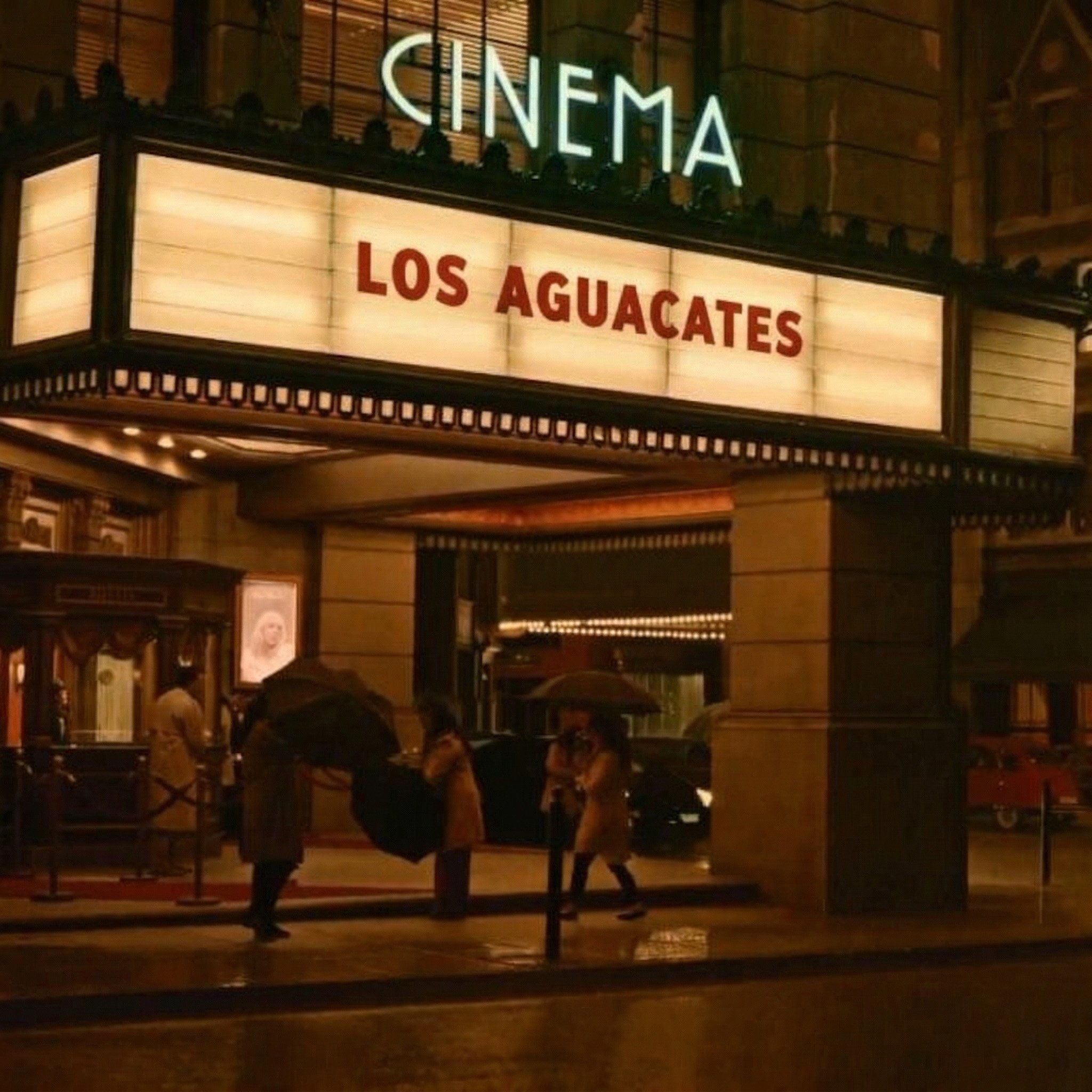 Cartelera de cine que anuncia la película "Los Aguacates", con personas con paraguas en la entrada en la noche.