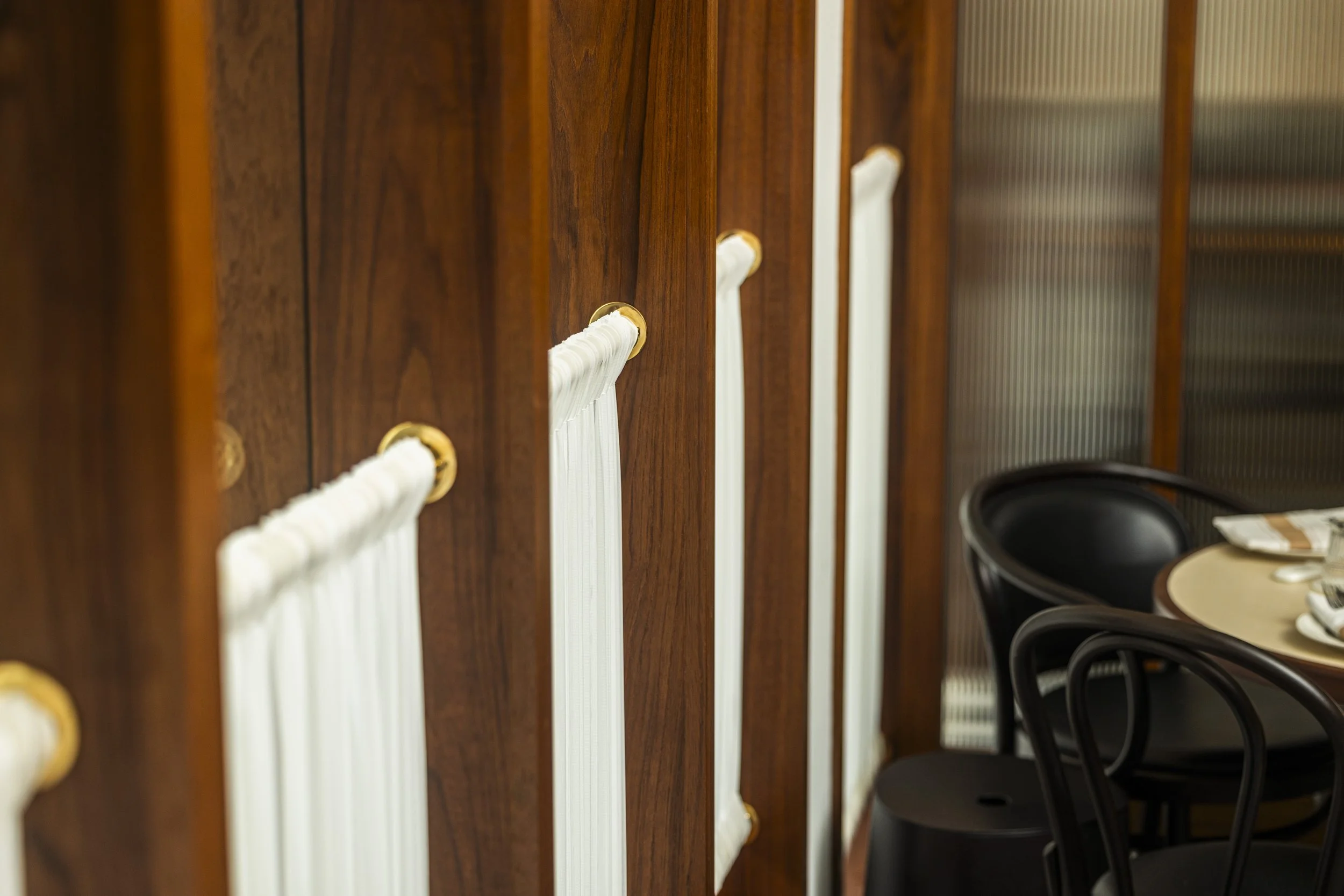 Close-up of hand sewn curtains mounted on a wooden wall, with a table and black chairs in the background at Chip Bee Bistro.