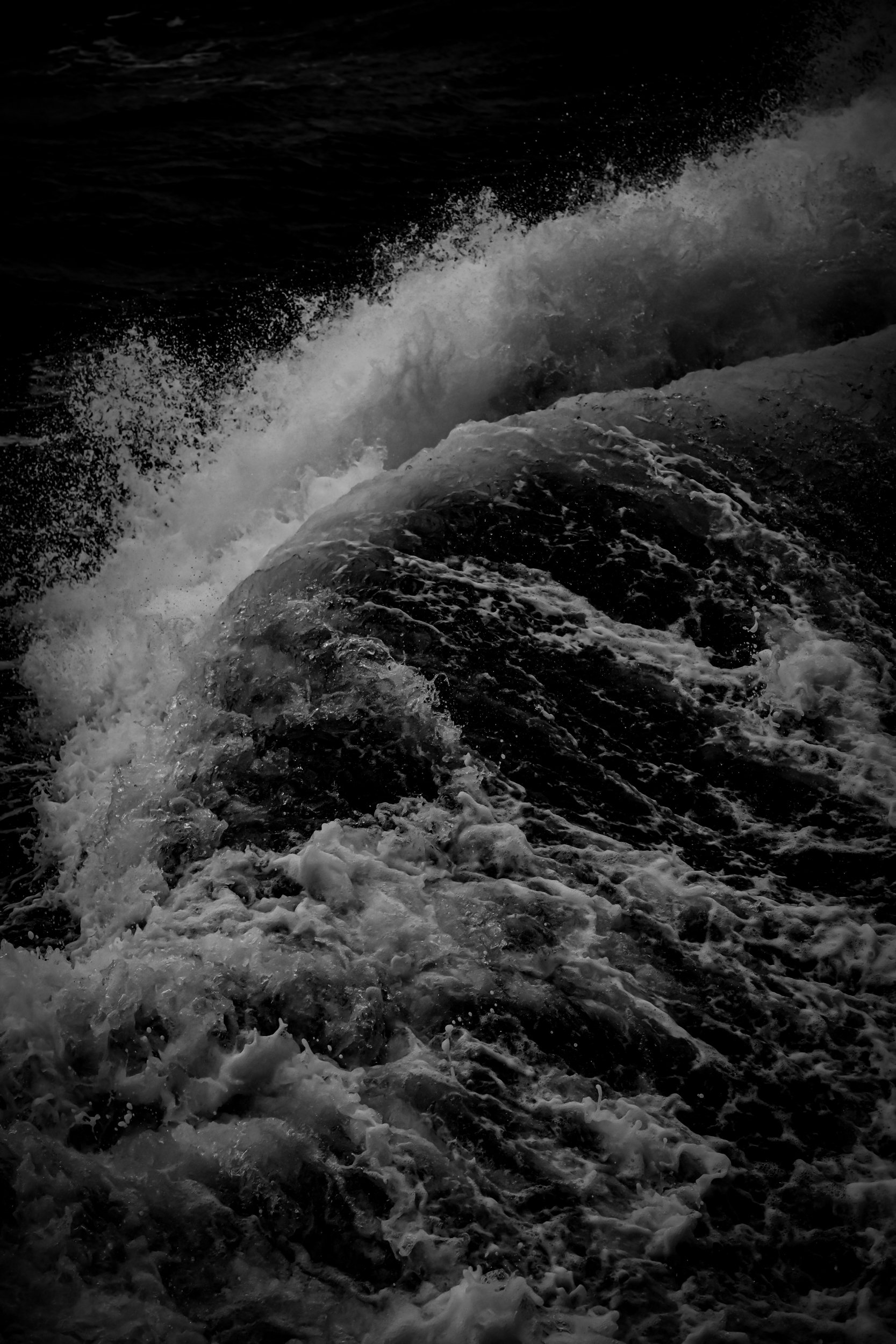 Black and white photograph of ocean waves crashing against rocks, creating foam and spray.
