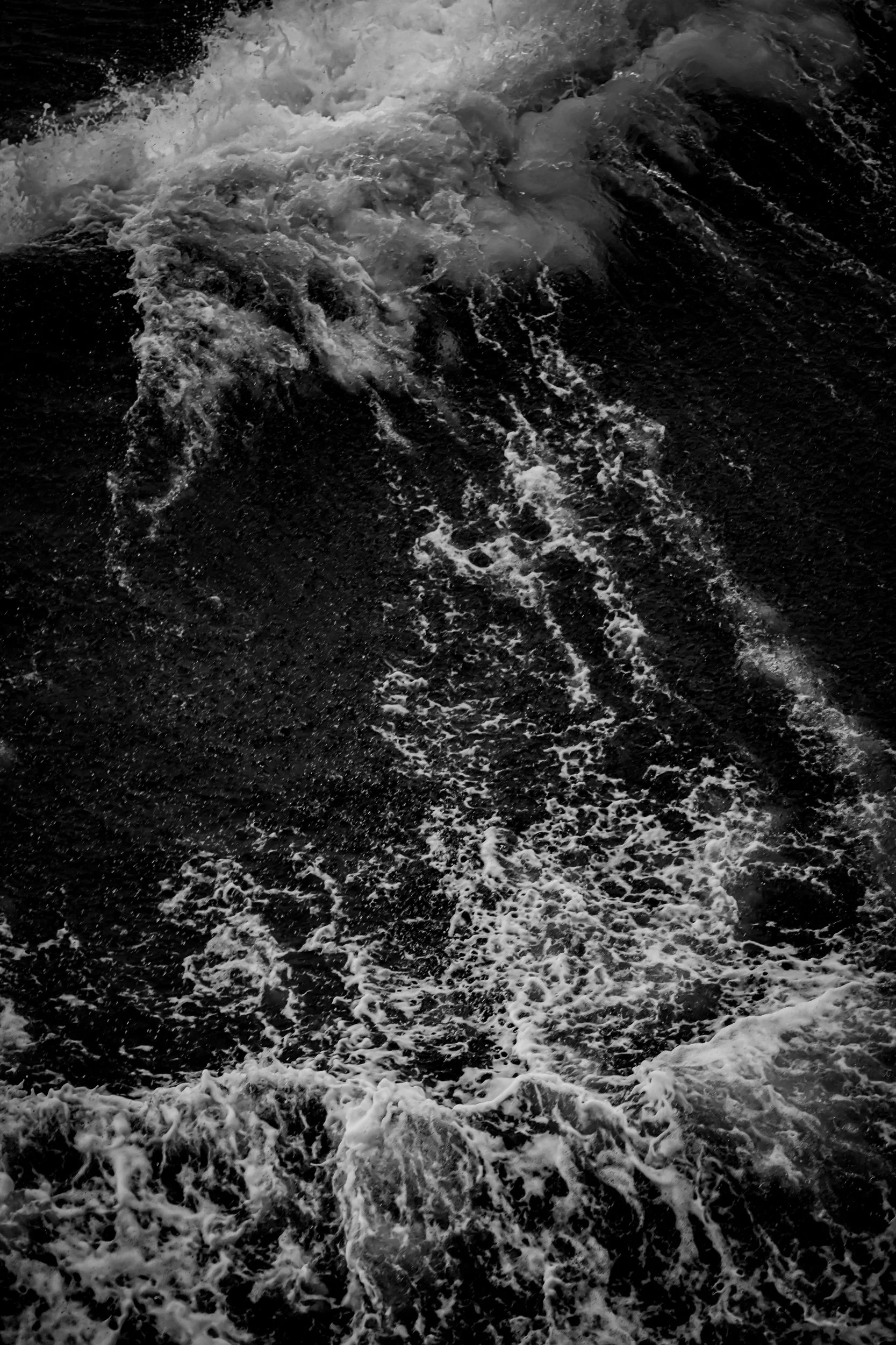 Close-up view of ocean waves and white foam on dark water.