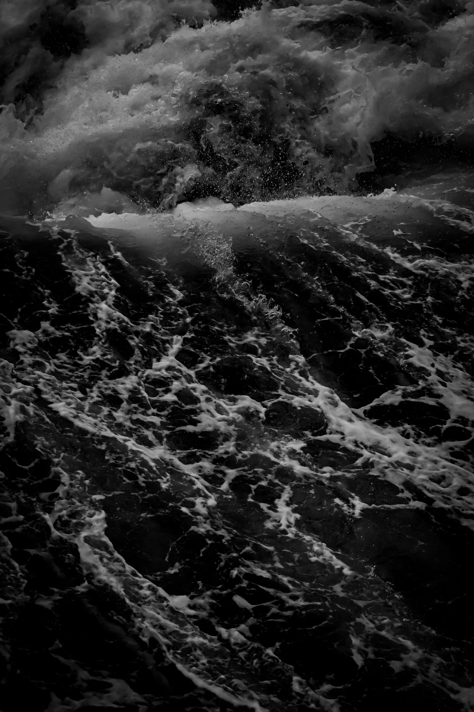 Black and white photograph of turbulent ocean waves with white foam on the surface.
