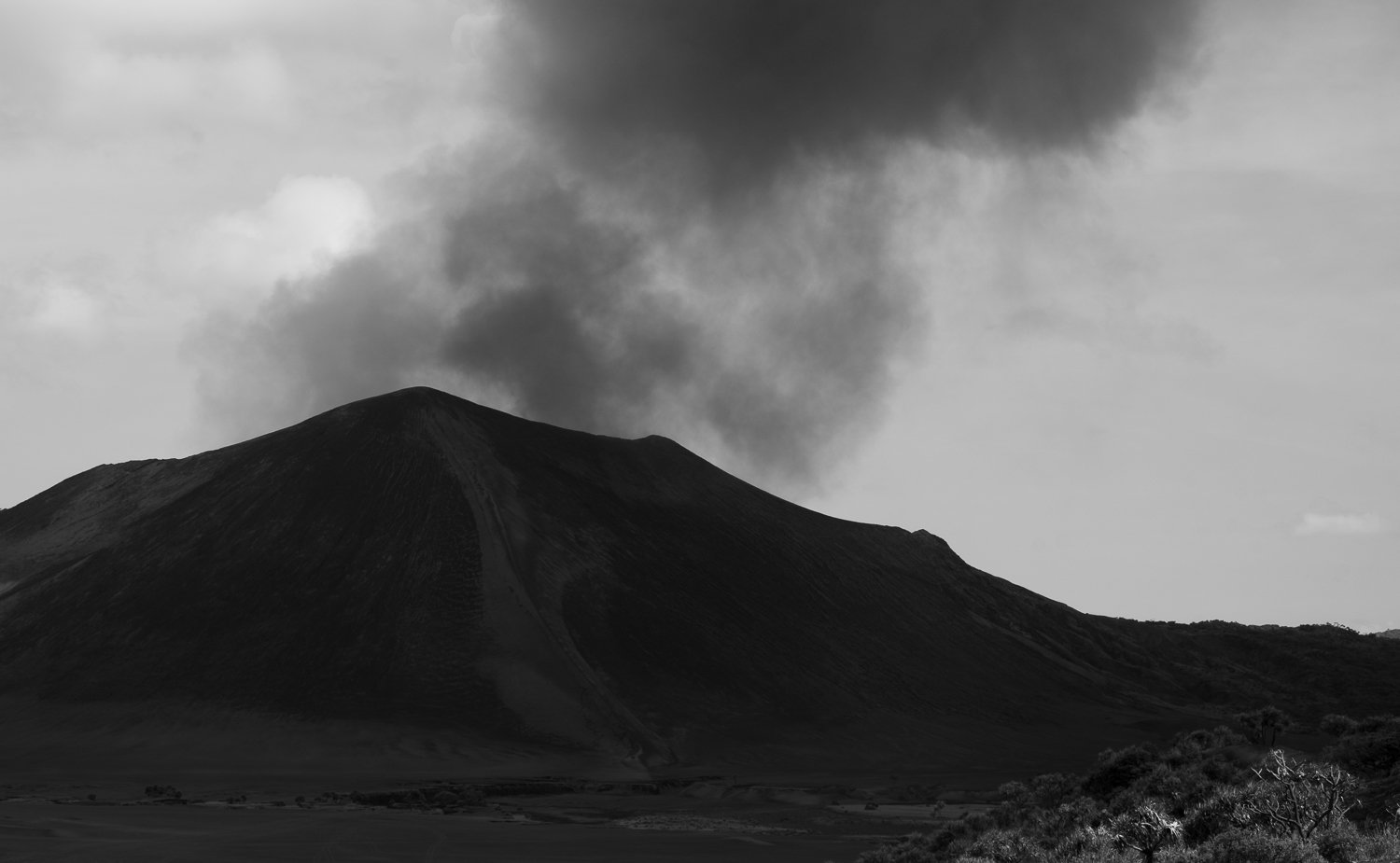 Black and white photo of a volcanic mountain erupting with smoke and ash rising from its summit.