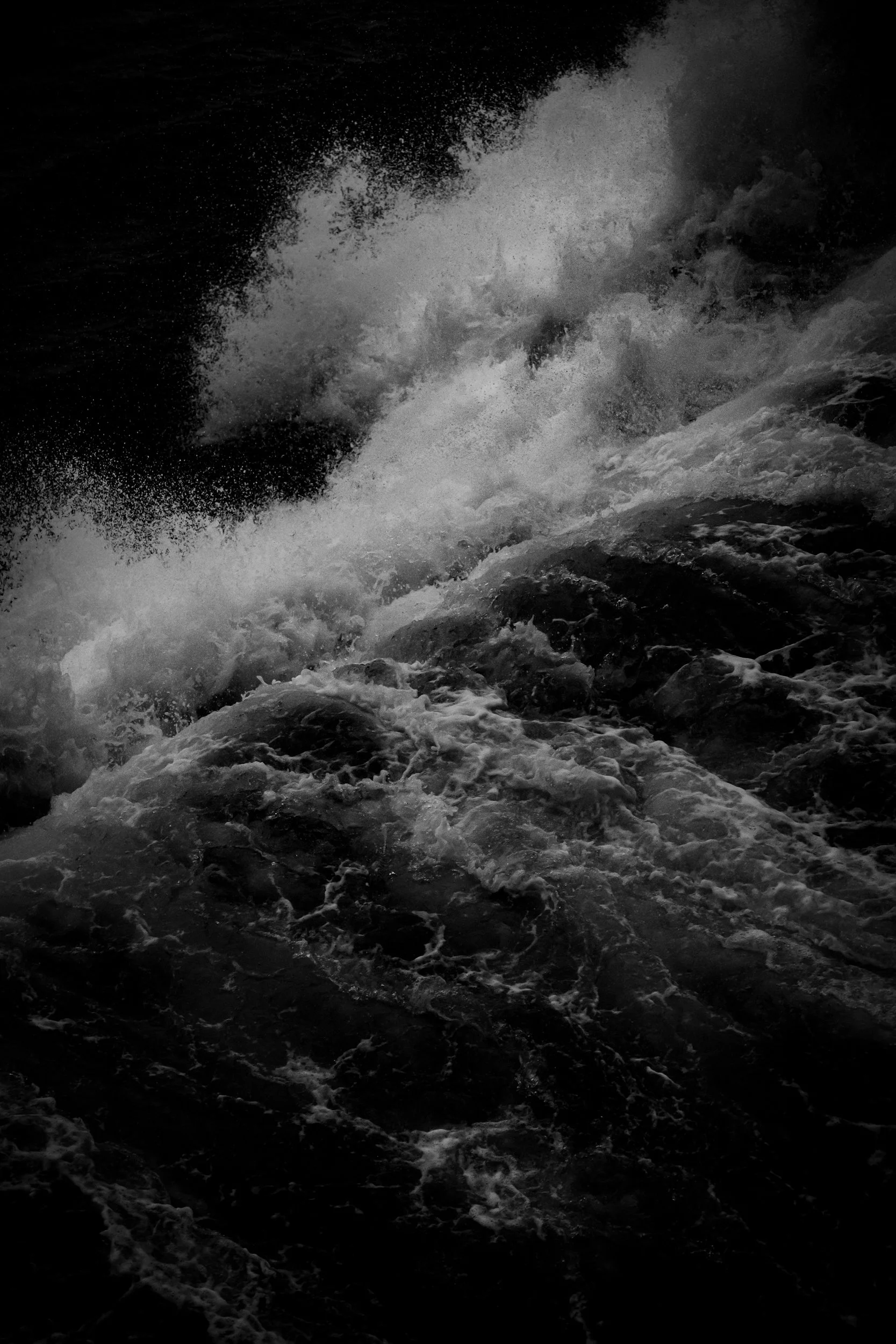Black and white photo of turbulent ocean waves crashing and splashing against rocks.