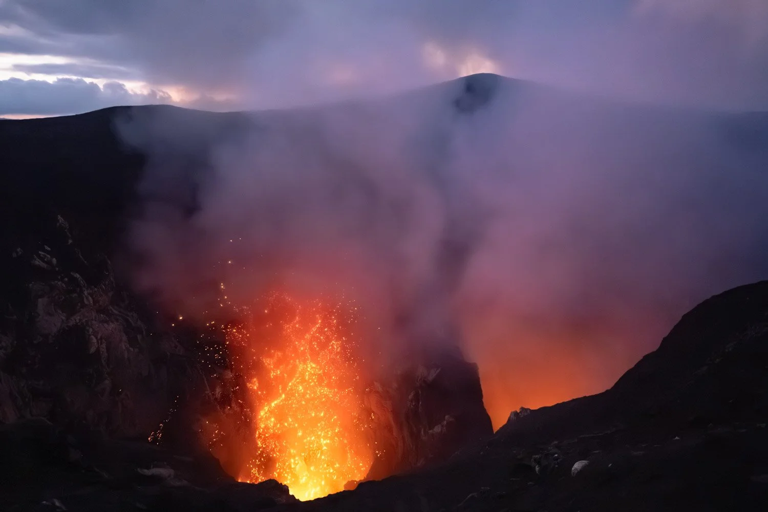 Erupting volcano spewing lava and smoke into the sky during twilight.