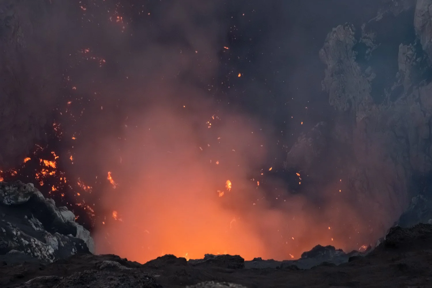 A view into a volcanic crater with flowing lava and smoke rising.