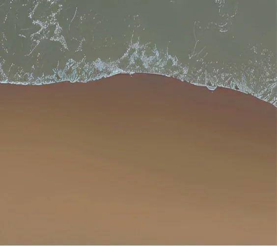 Aerial view of a beach showing ocean waves approaching the sandy shoreline.