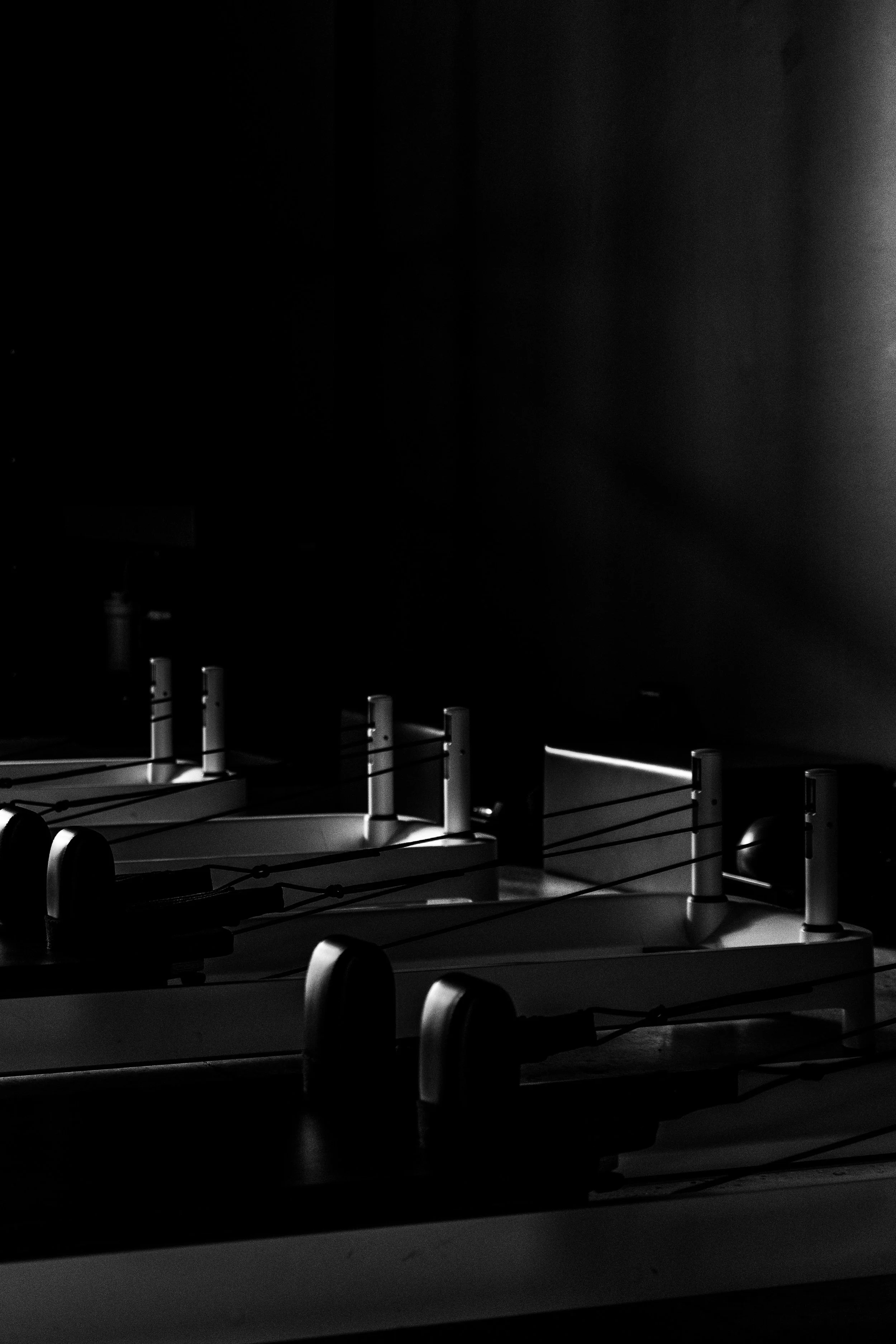 Black and white photo of pilates equipment in a dark room with minimal lighting.