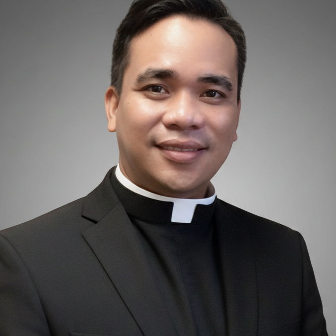 A smiling man dressed as a Catholic priest, wearing a black clergy shirt with a white clerical collar.