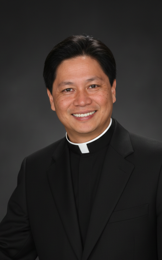 A smiling man dressed in a black clergy shirt with a white collar, wearing a black suit jacket, against a dark gray background.