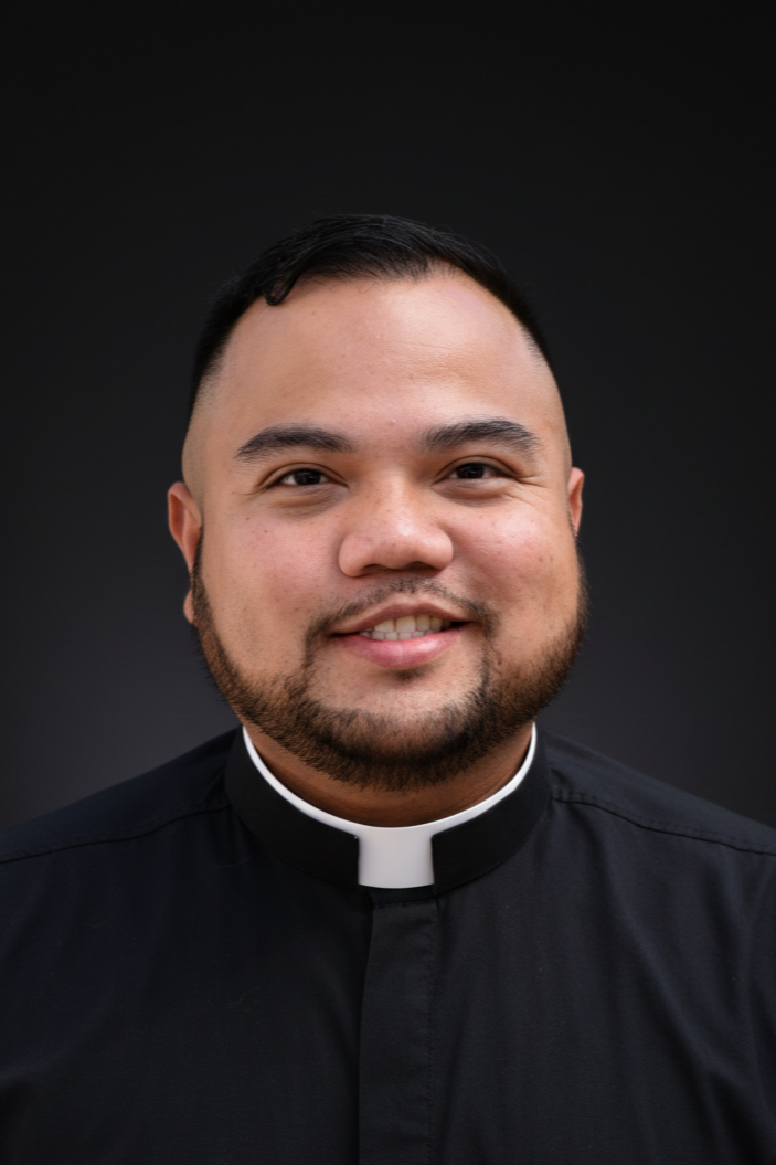 Portrait of a smiling man wearing a black clergy shirt with a white clerical collar, set against a dark background.