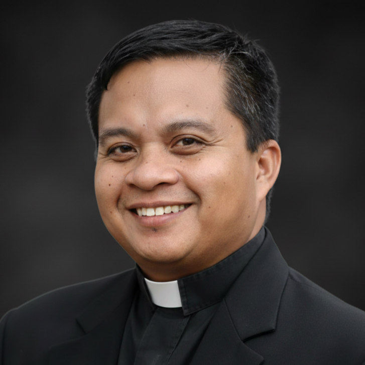Close-up of a smiling male priest in black clerical clothing with a white collar, against a dark blurred background.