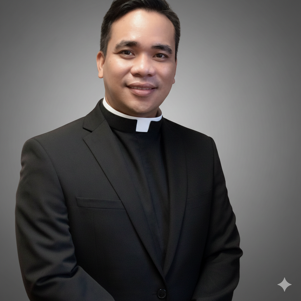 A young man dressed in a black clerical suit with a white clerical collar, smiling and looking at the camera against a plain gray background.