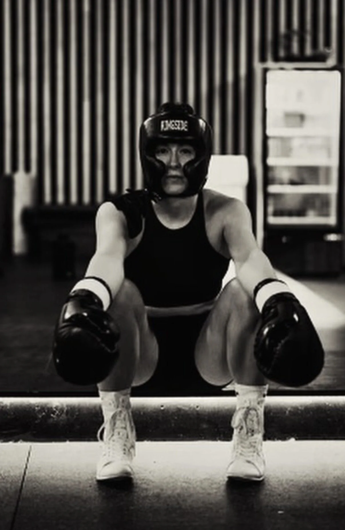 Two ladies with white sports bras on training in a boxing ring,  o ne is holding mitts while the other is punching