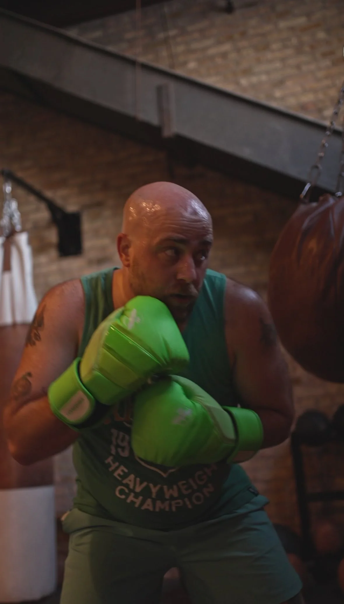 A boxer getting ready to throw a punch on a heavy bag.  He's wearing bright green gloves and a green tank top