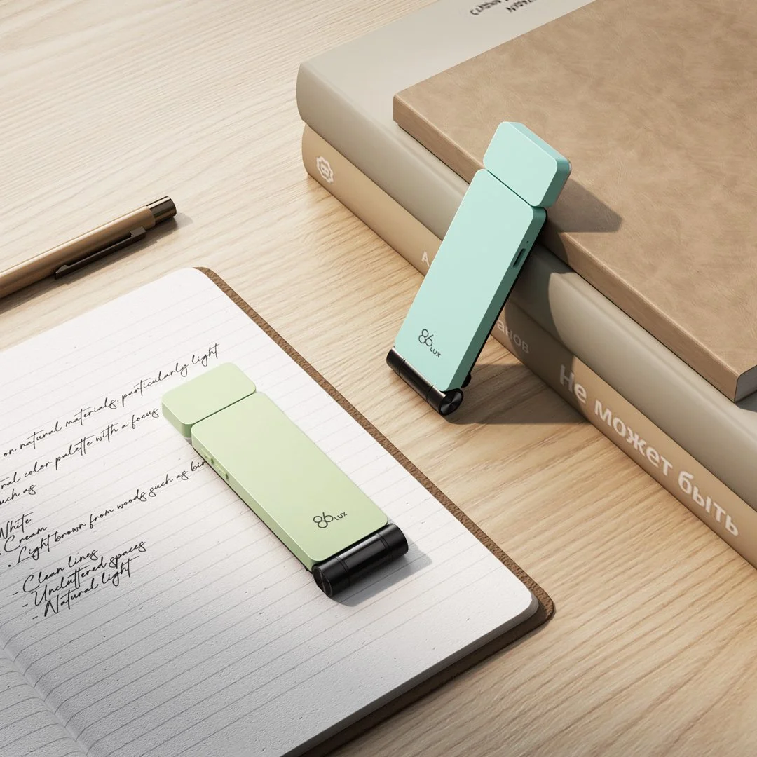 Two small, light green portable projectors on a wooden desk, one placed on an open notebook with handwritten notes, and the other leaning against a stack of books.