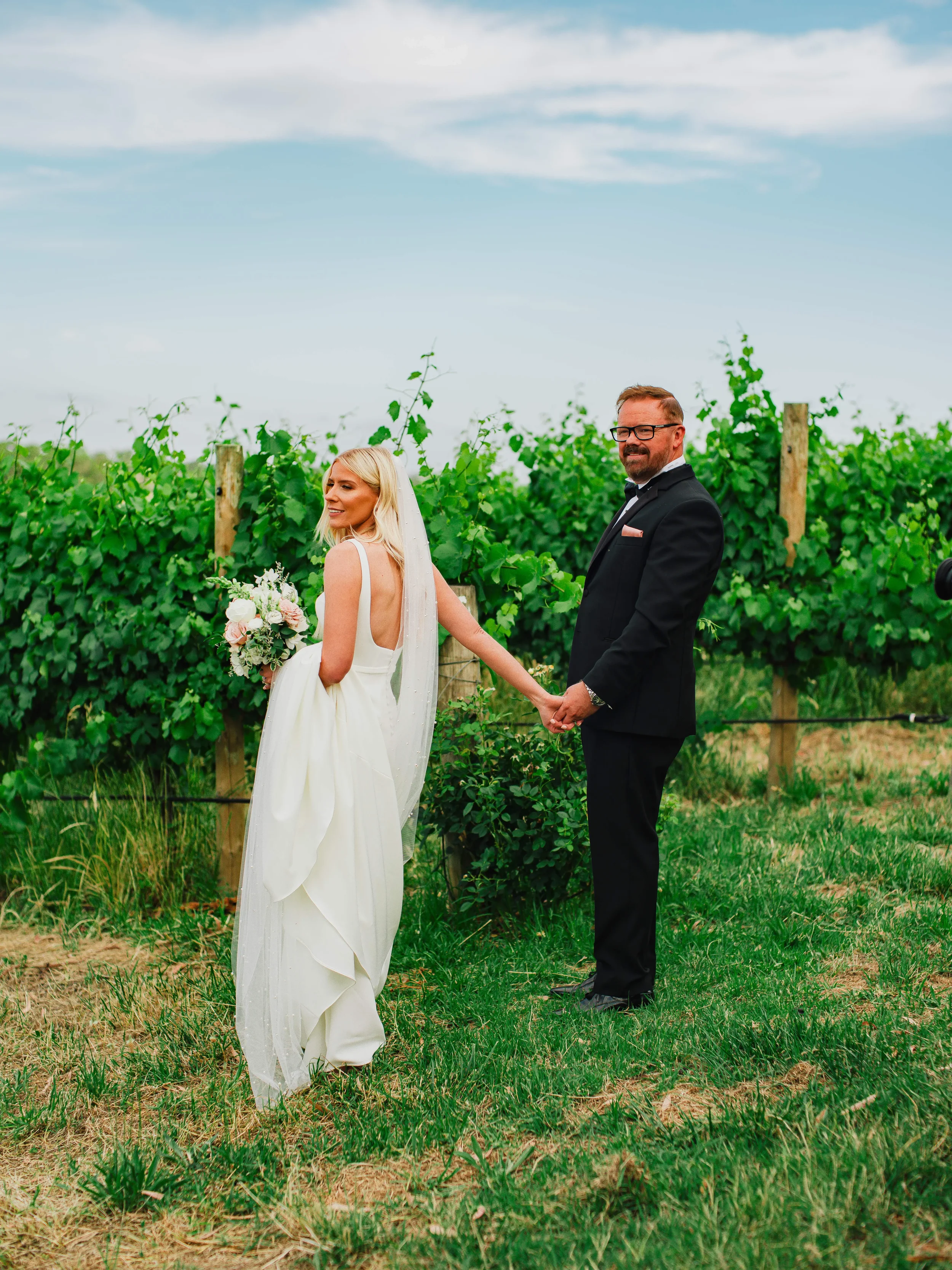Bride and groom holding hands among vineyard rows during an outdoor wedding photography session.