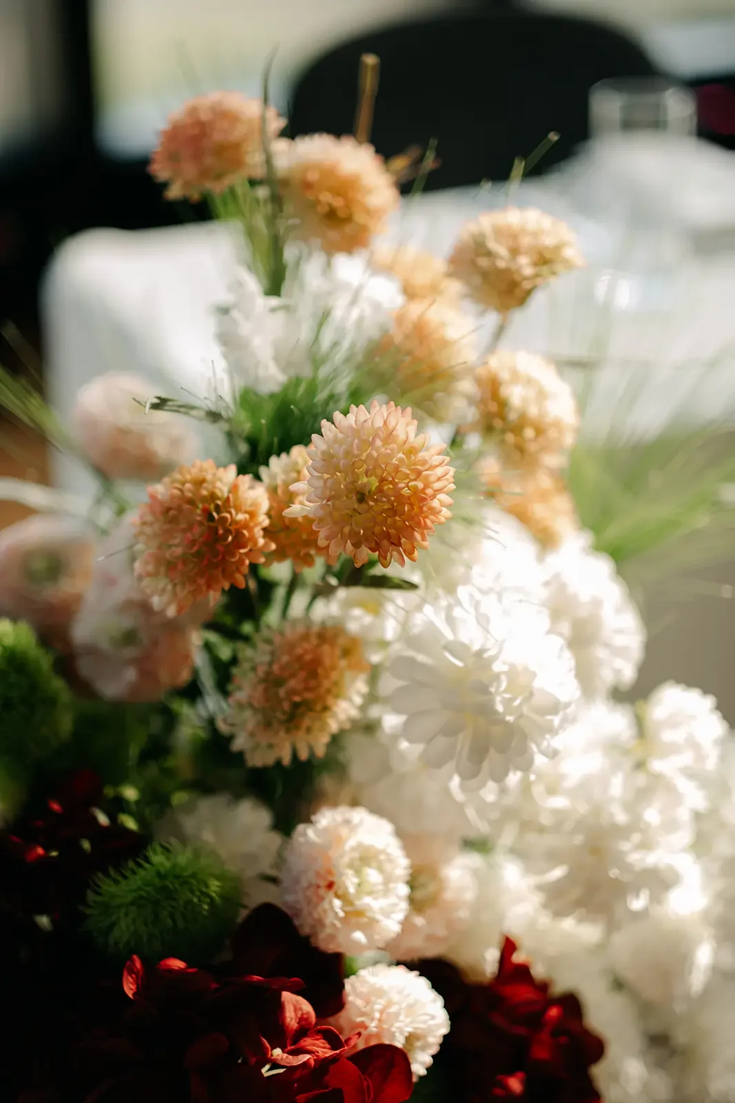 Elegant wedding floral arrangement with peach, white and deep red flowers captured in natural light.