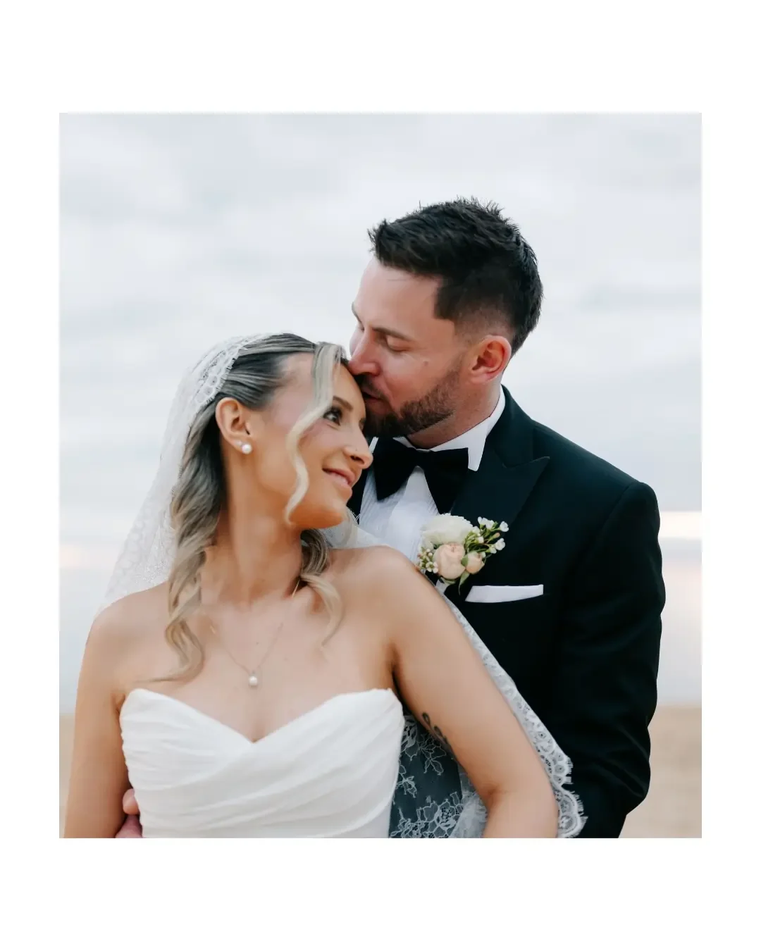 Groom kissing the bride on the forehead during a romantic outdoor wedding portrait.