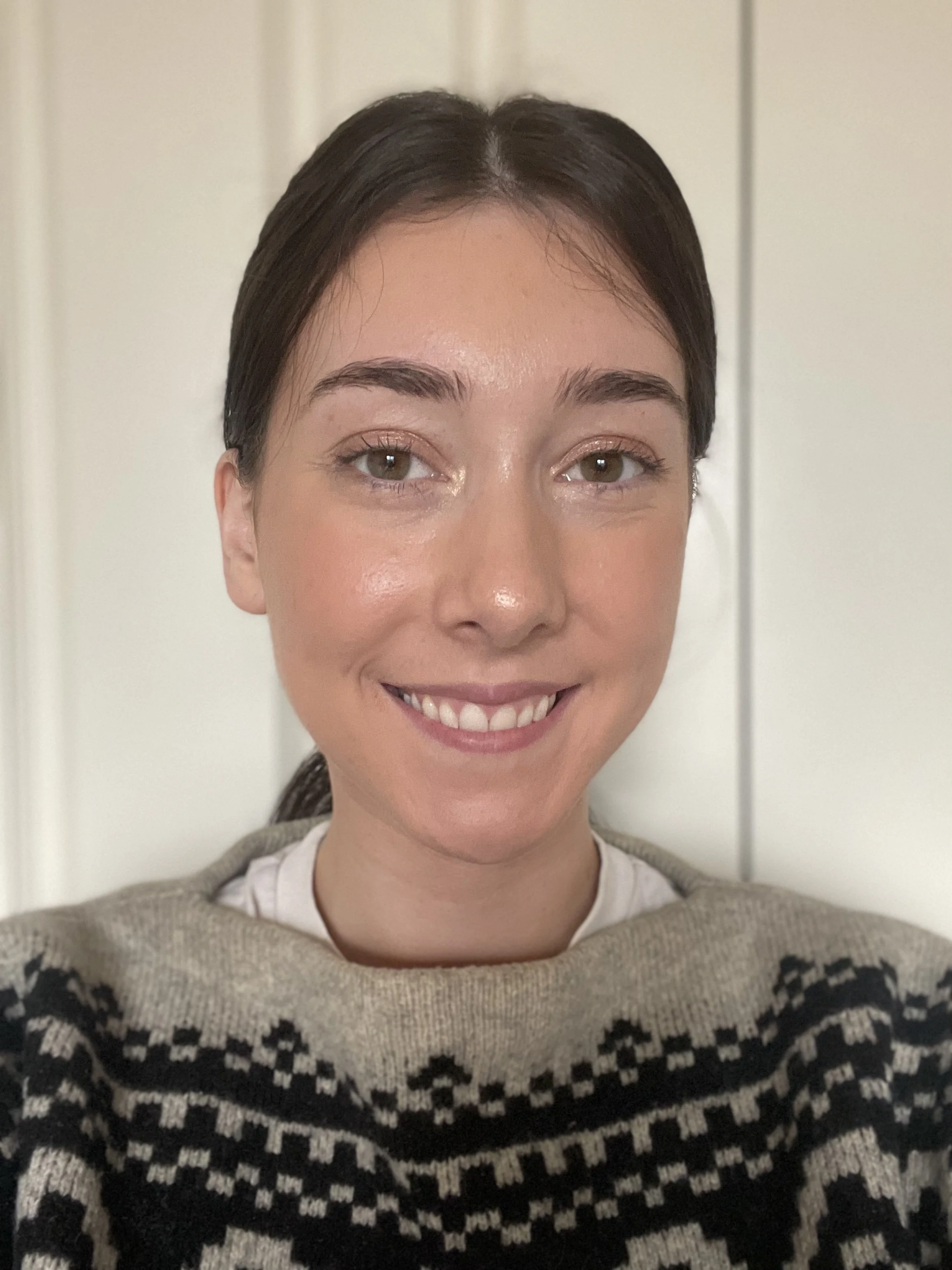 An image of Louise Blair-West smiling at the camera. She is wearing a white shirt with a grey and black jumper over the top.