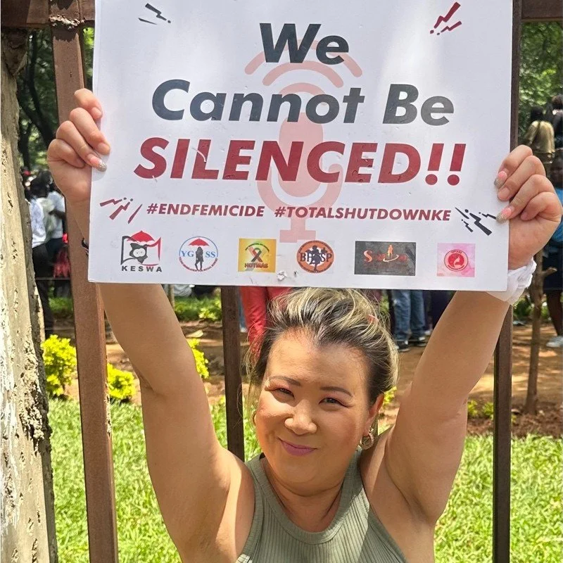 An image of Sarah Chong in a green singlet. She is holding a sign that says "We Cannot Be Slienced!! #ENDFEMICIDE #TOTALSHUTDOWNKE."