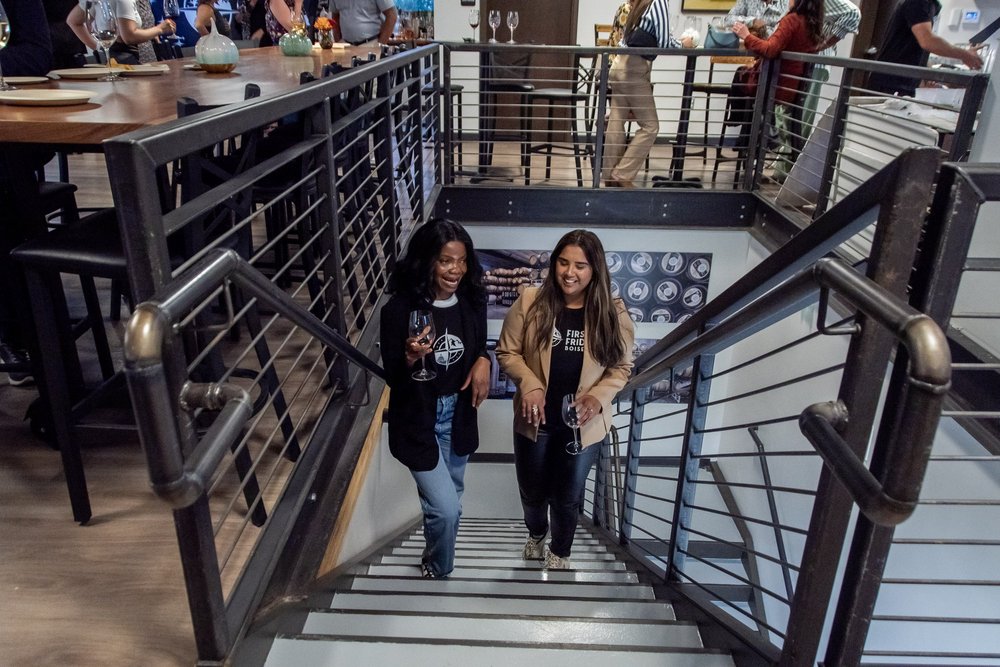 Two women talking and laughing on the stairs at a First Fridays Boise gathering