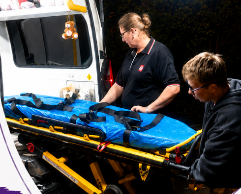 Two people pushing an ambulance trolley into ambulance. 