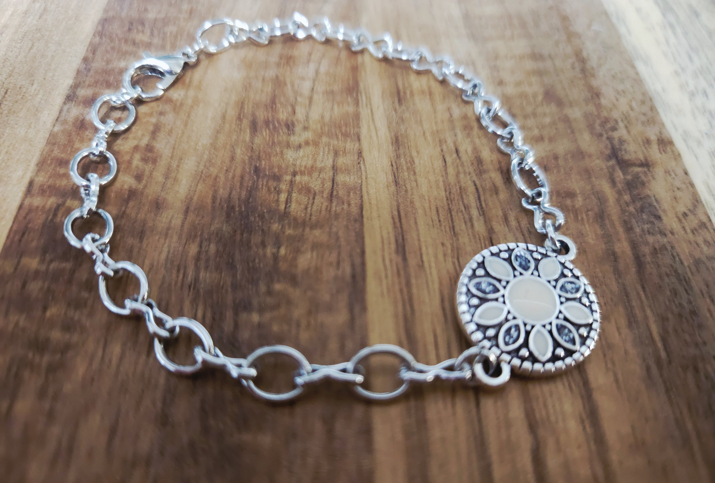 silver bracelet with a white enamel concho centerpiece with a floral and wood design in the background