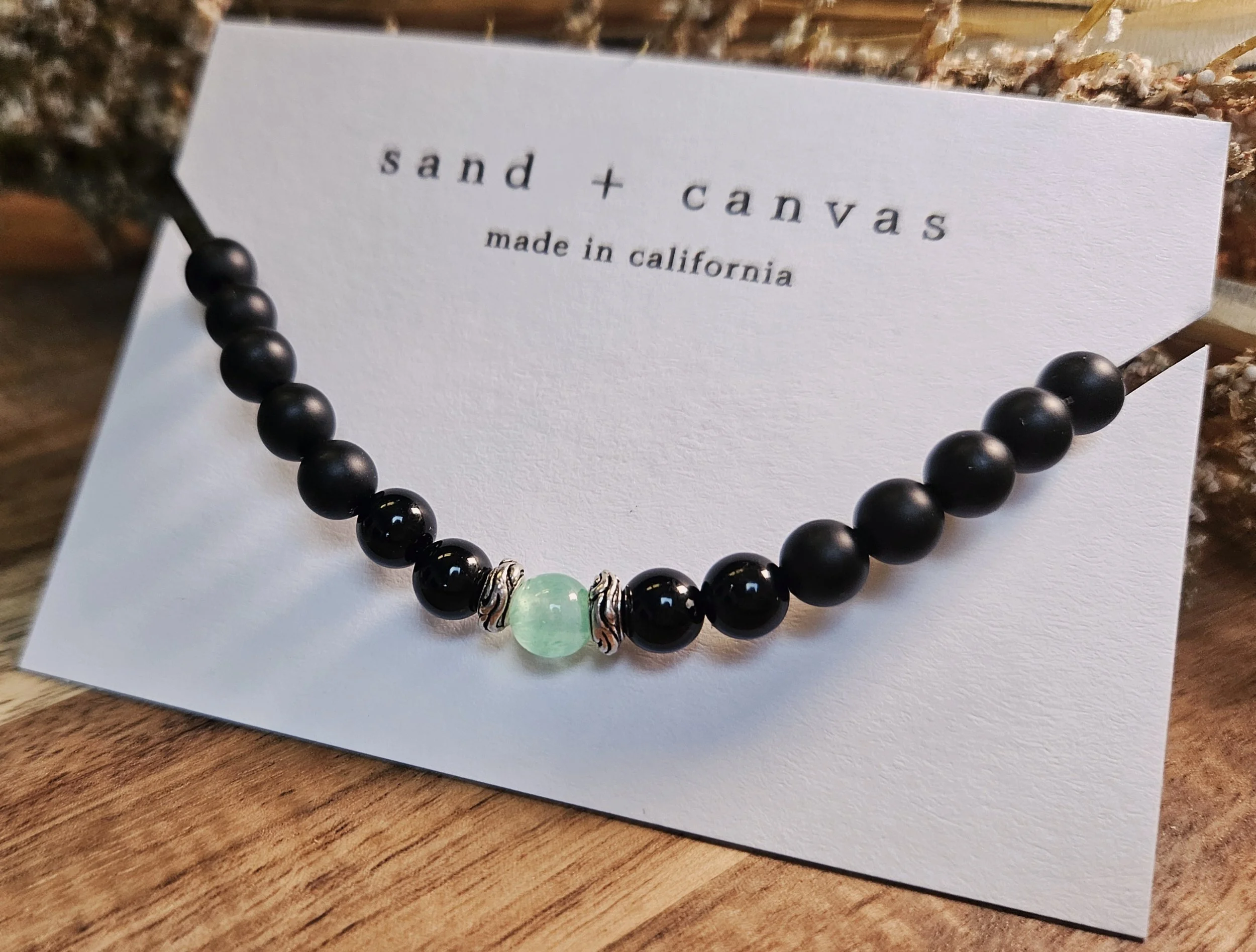 black and green chakra bracelet on a product card for sand and canvas