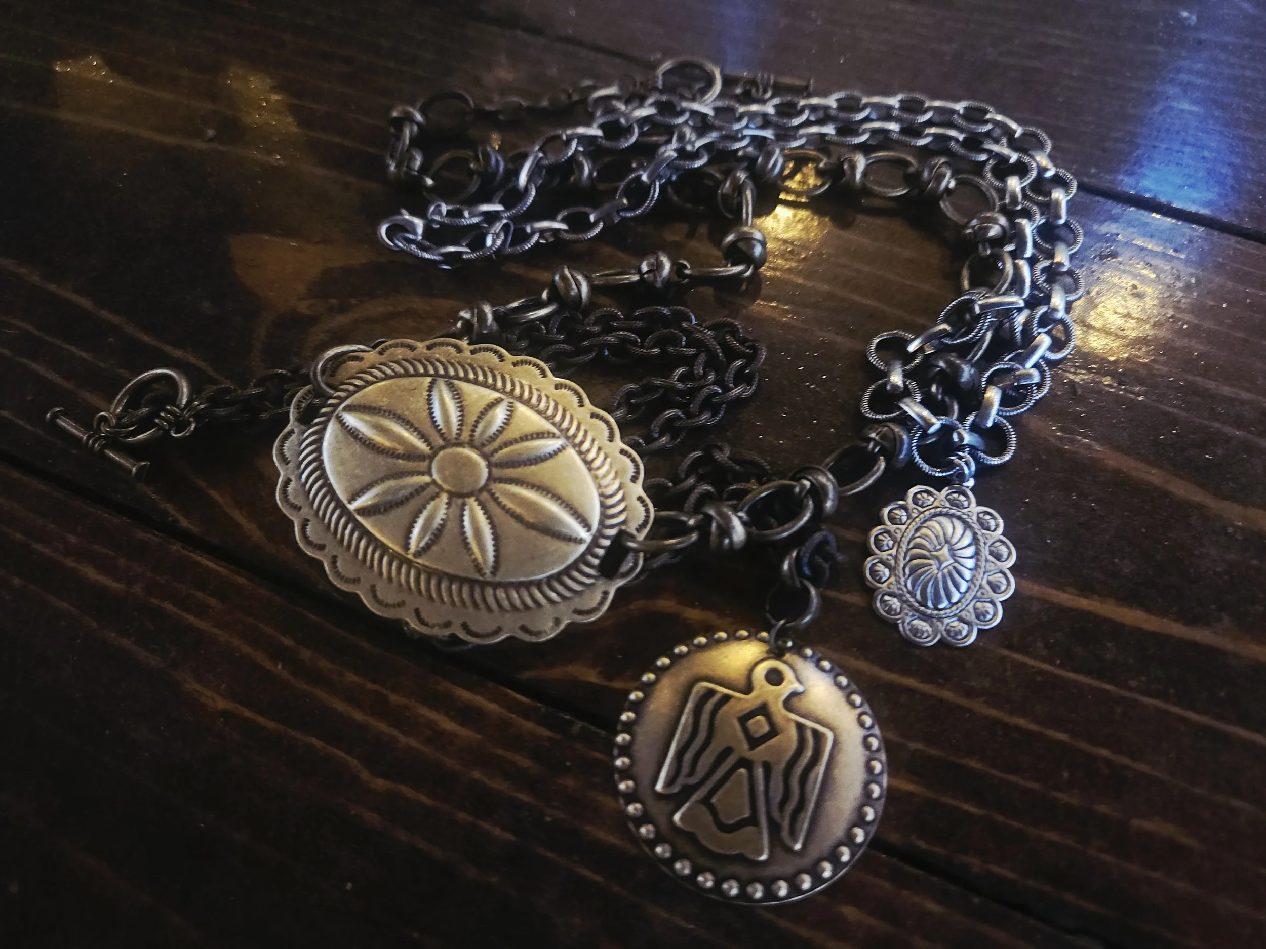 Mixed metal silver and brass concho necklaces layered on a wood background for sand and canvas