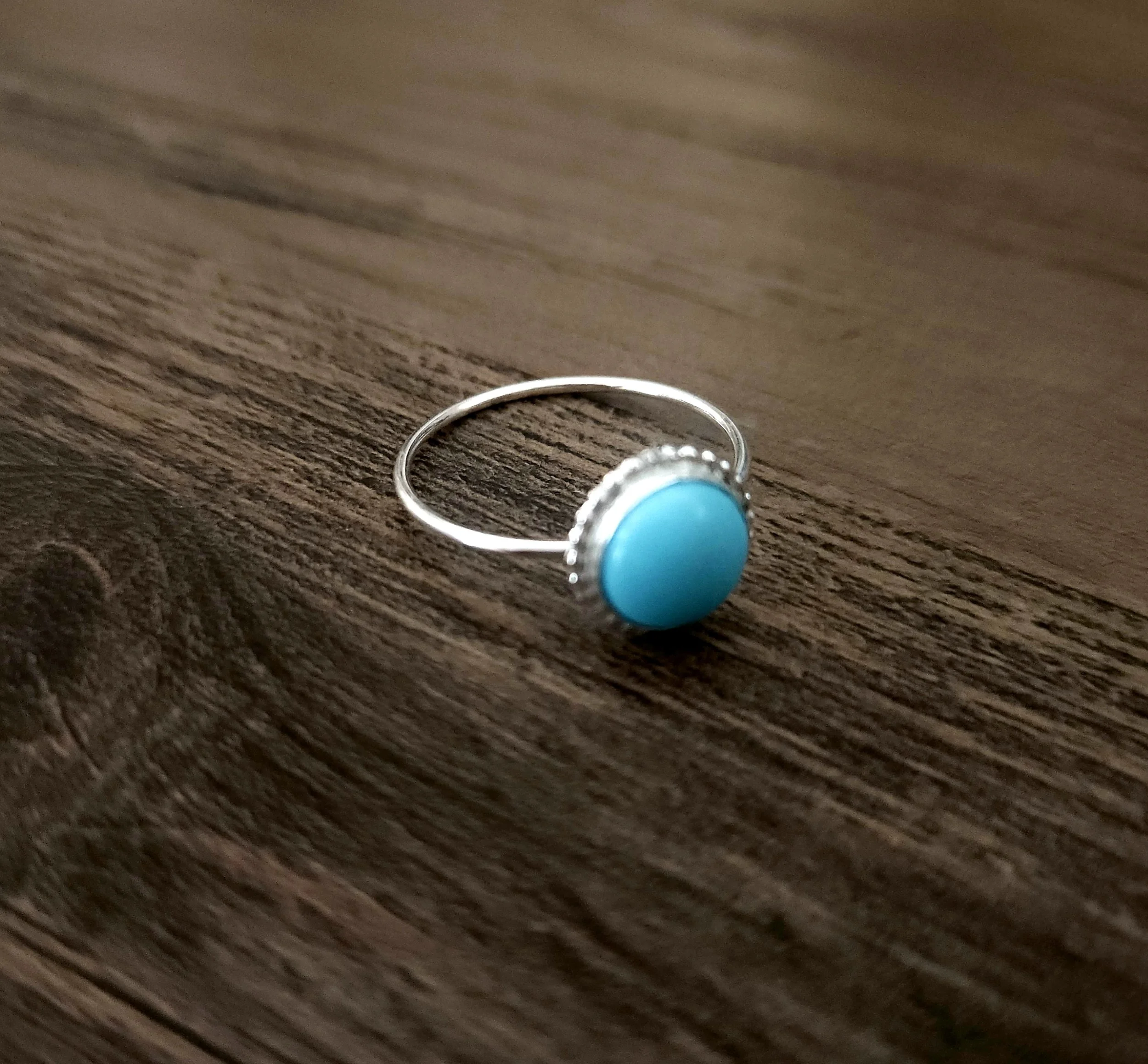 Turquoise and silver ring with beaded edging sand and canvas on a wood table