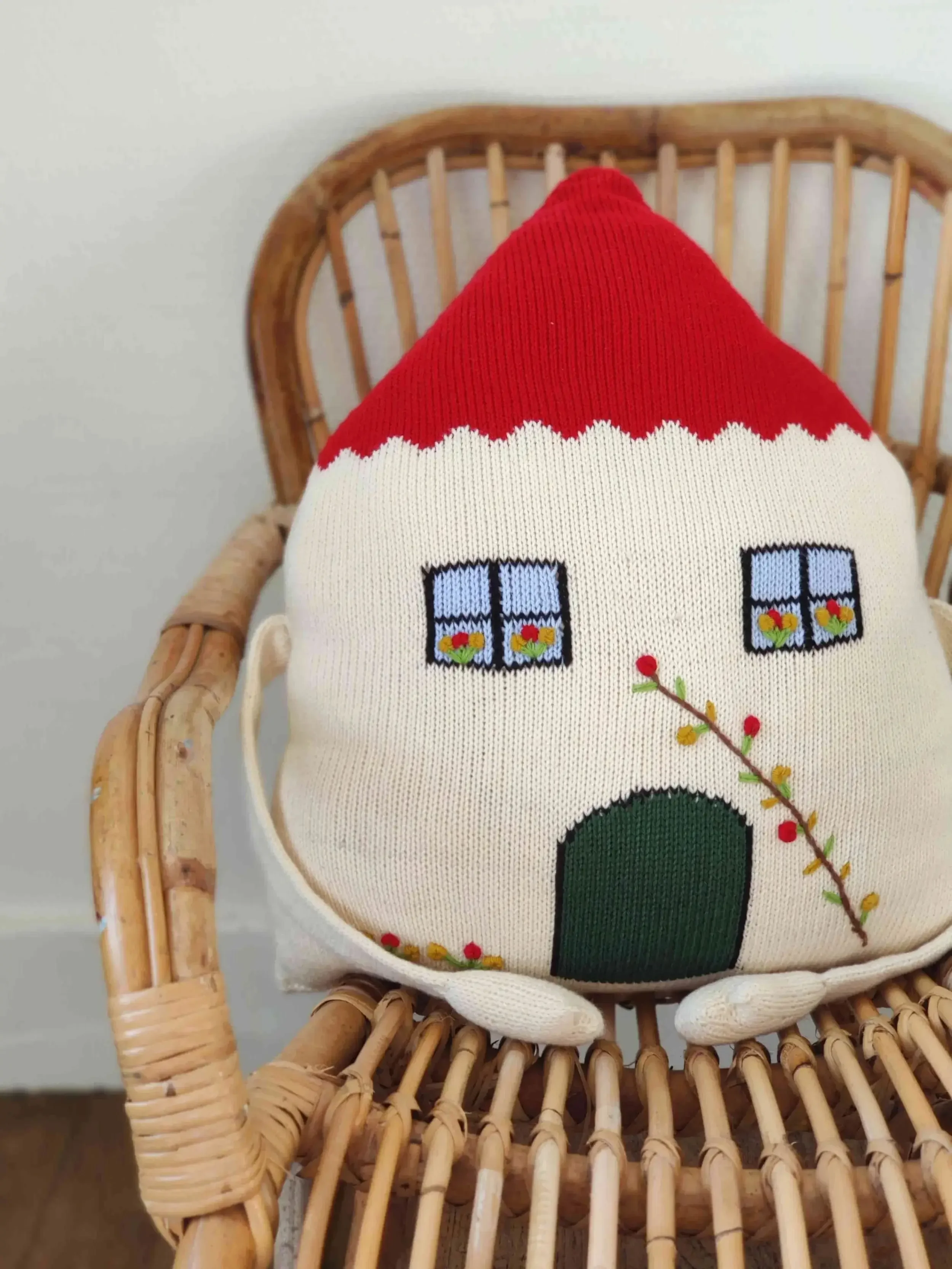 Coussin Maison du Réconfort tricoté en coton bio, sur une chaise en osier. Cadeau symbolique
