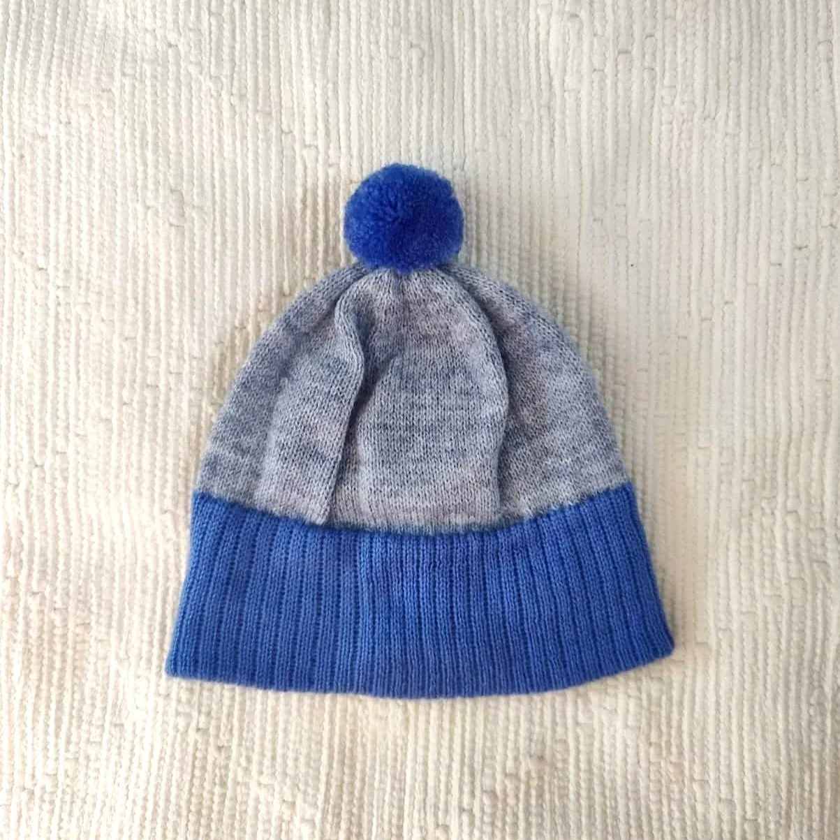Bonnet artisanal tricoté en laine gris avec pompon et revers bleus pour enfant