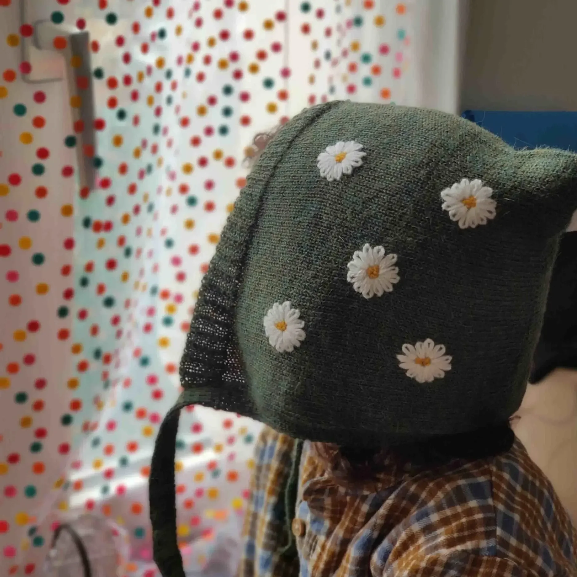 Bébé portant un bonnet béguin en alpaga vert avec des broderies de marguerite