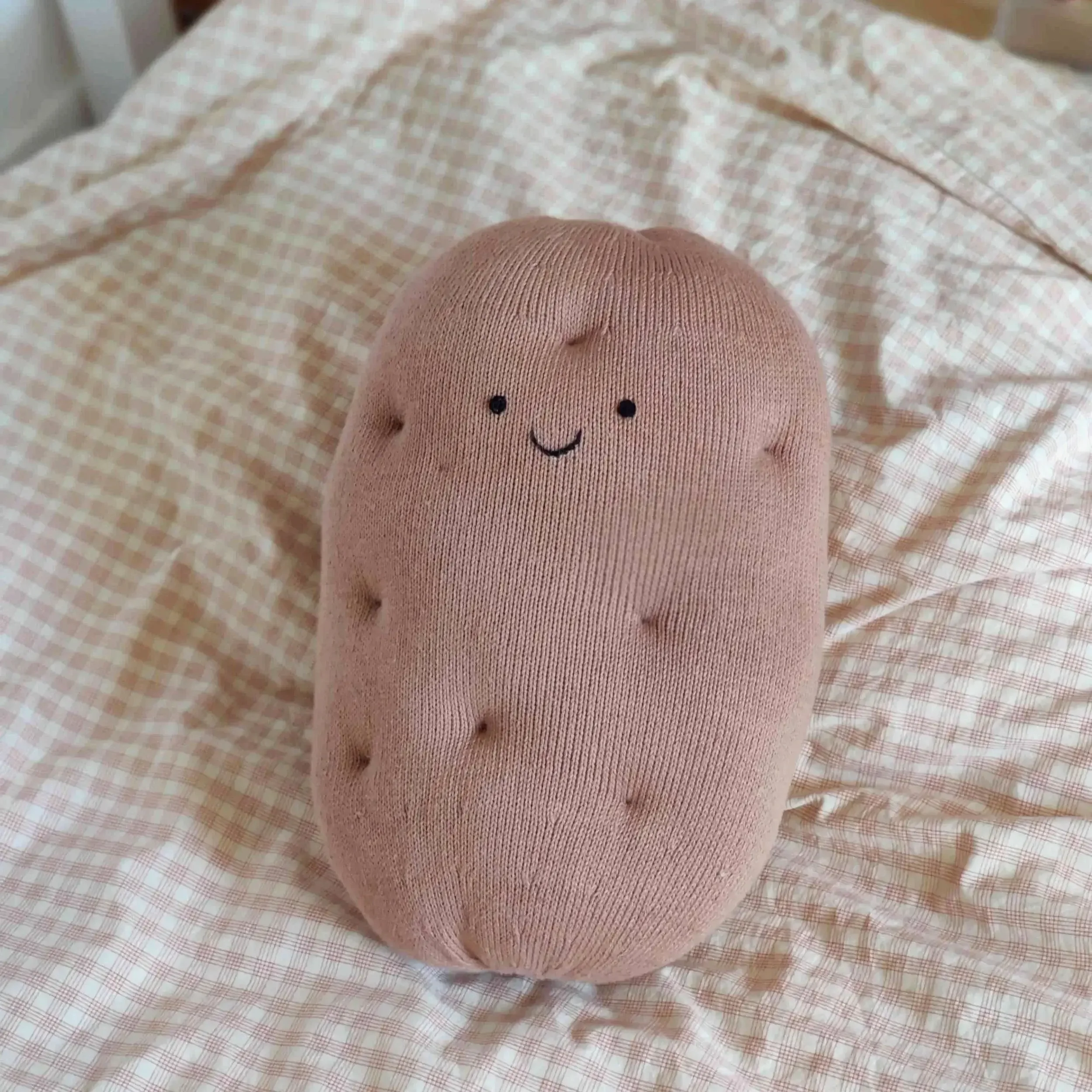 Coussin Pomme de Terre tricoté en coton bio sur un lit. Cadeau symbolique artisanal.