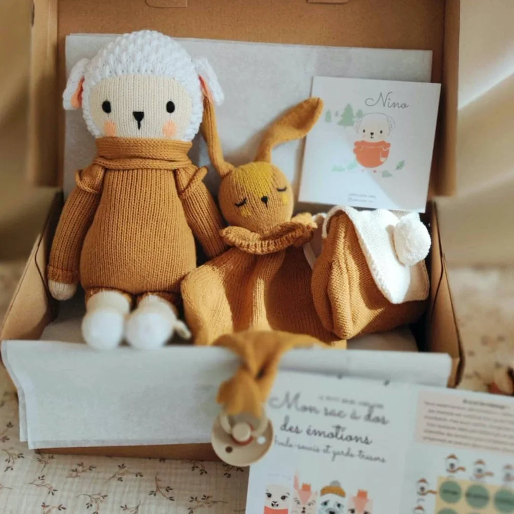 Coffret naissance Nino Caramel le Mouton avec la peluche des émotions Nino Caramel, son sac à dos des émotions à pompon et le doudou attache-tétine dans sa boîte cadeau