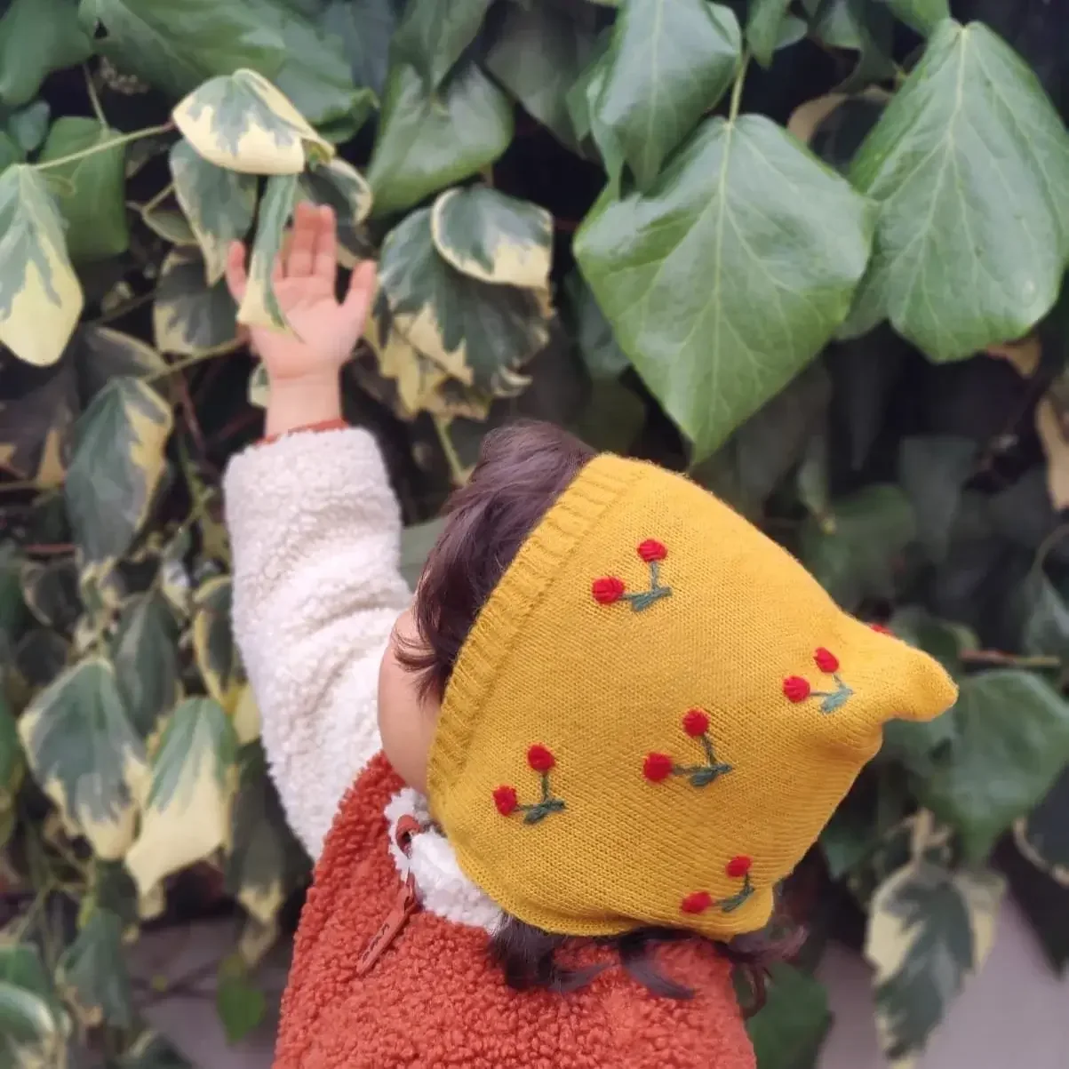 Bébé portant un bonnet béguin en alpaga jaune avec des broderies de cerise