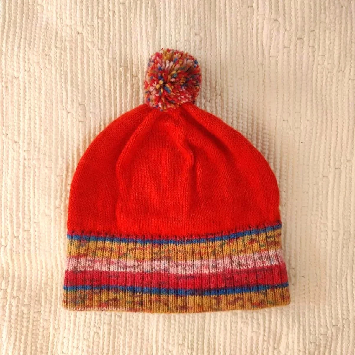 Bonnet artisanal tricoté en laine rouge avec pompon et revers multicolores à motifs pour enfant