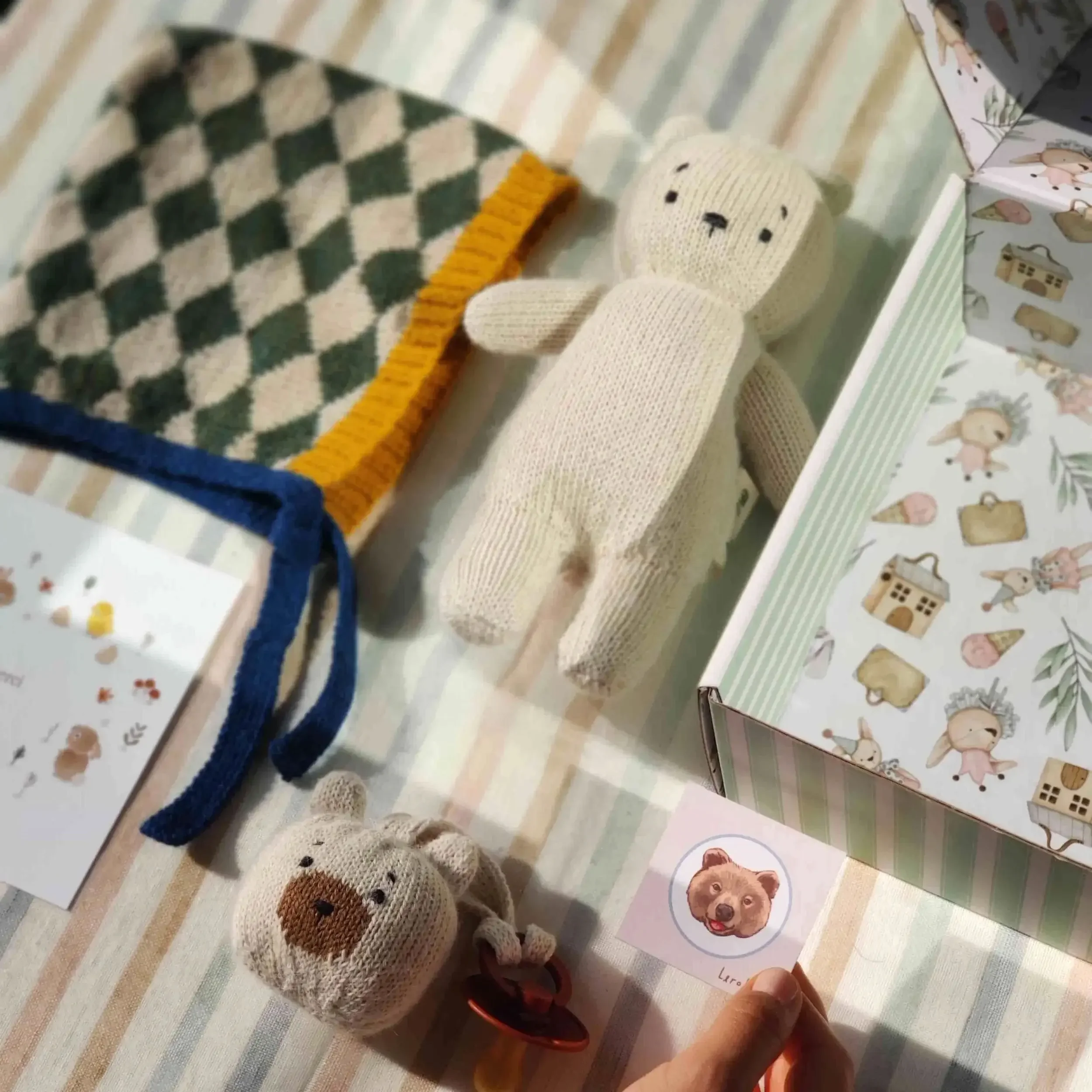 Composition du coffret naissance Alpaga neige : un ourson Teddy Bear en alpaga blanc, un mini-Teddy attache-tétine en alpaga blanc et un bonnet béguin avec motifs losange verts et blancs