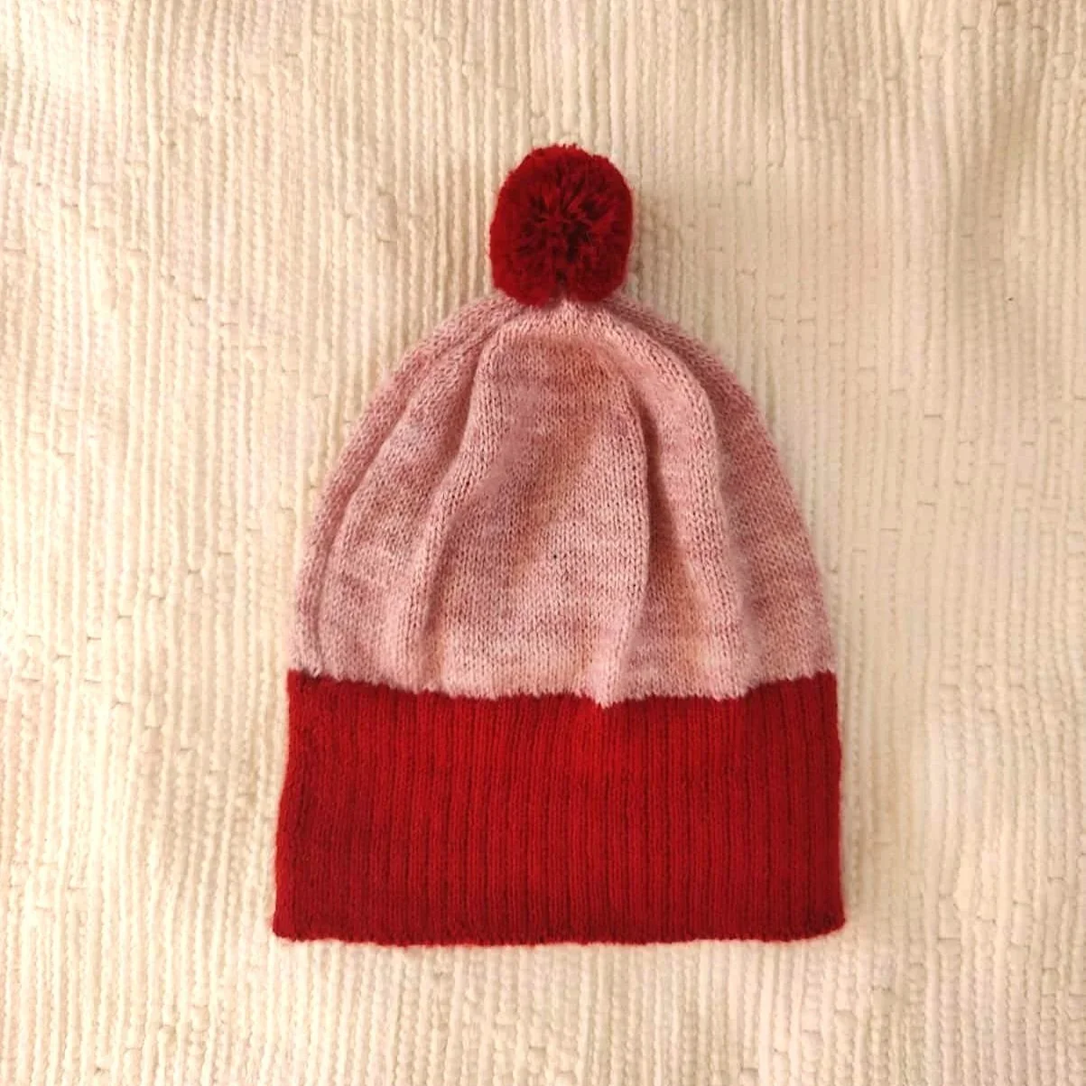 Bonnet artisanal tricoté en laine rose avec pompon et revers rouges pour enfant