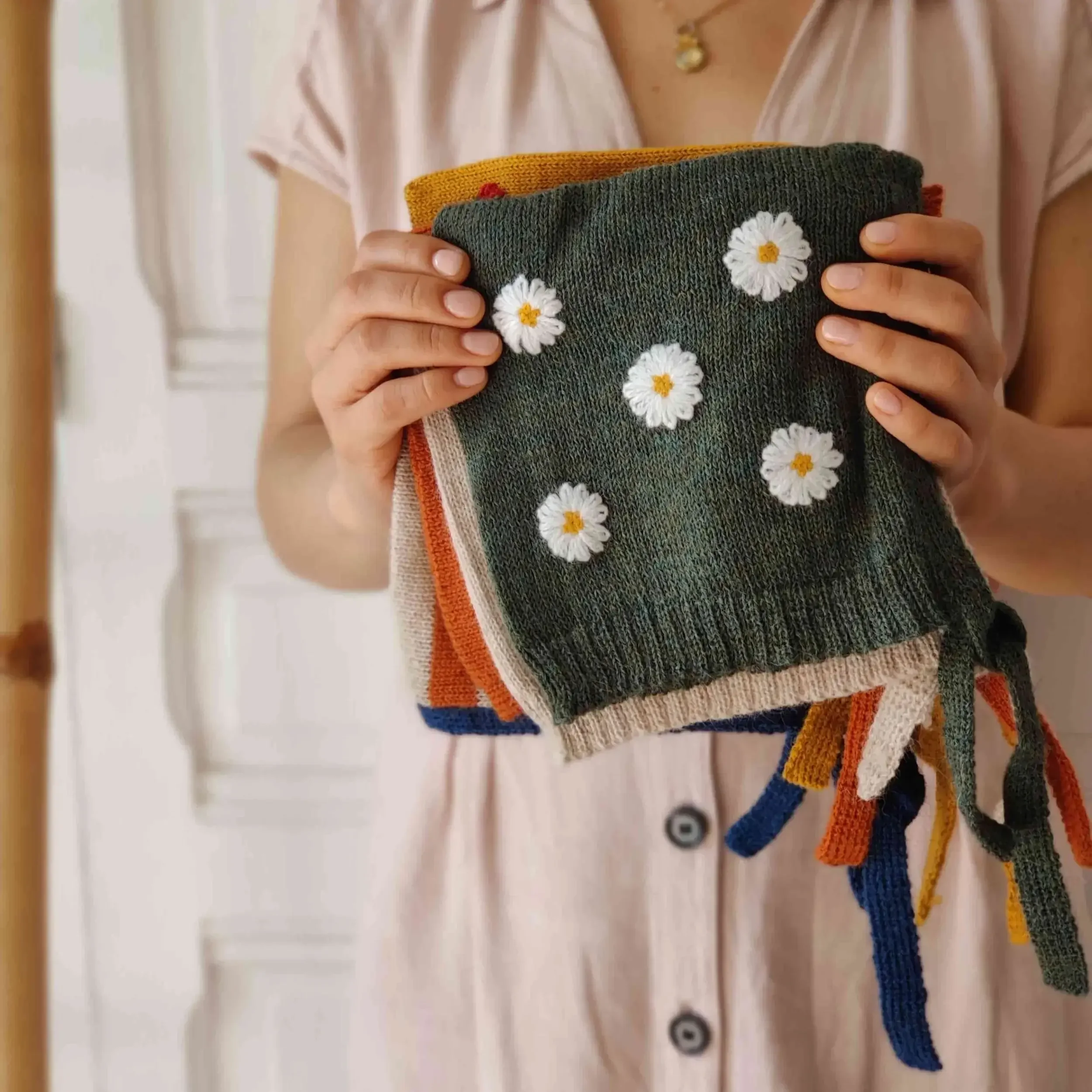 Maman qui présente dans ses mains le modèle de bonnet béguin en alpaga avec les broderies de marguerite
