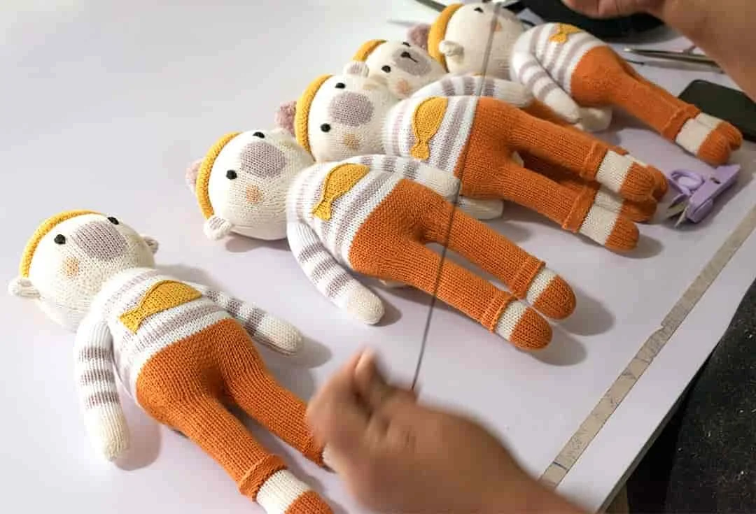 Peluches des émotions en coton bio alignées sur une table d'atelier avec un artisan qui tricote