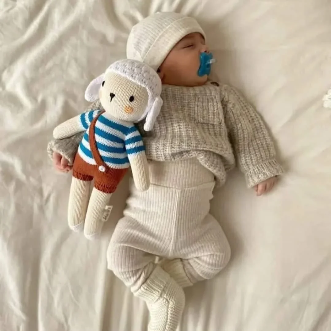 Bébé qui dort paisiblement avec sa peluche mouton Nino Marin à côté de lui
