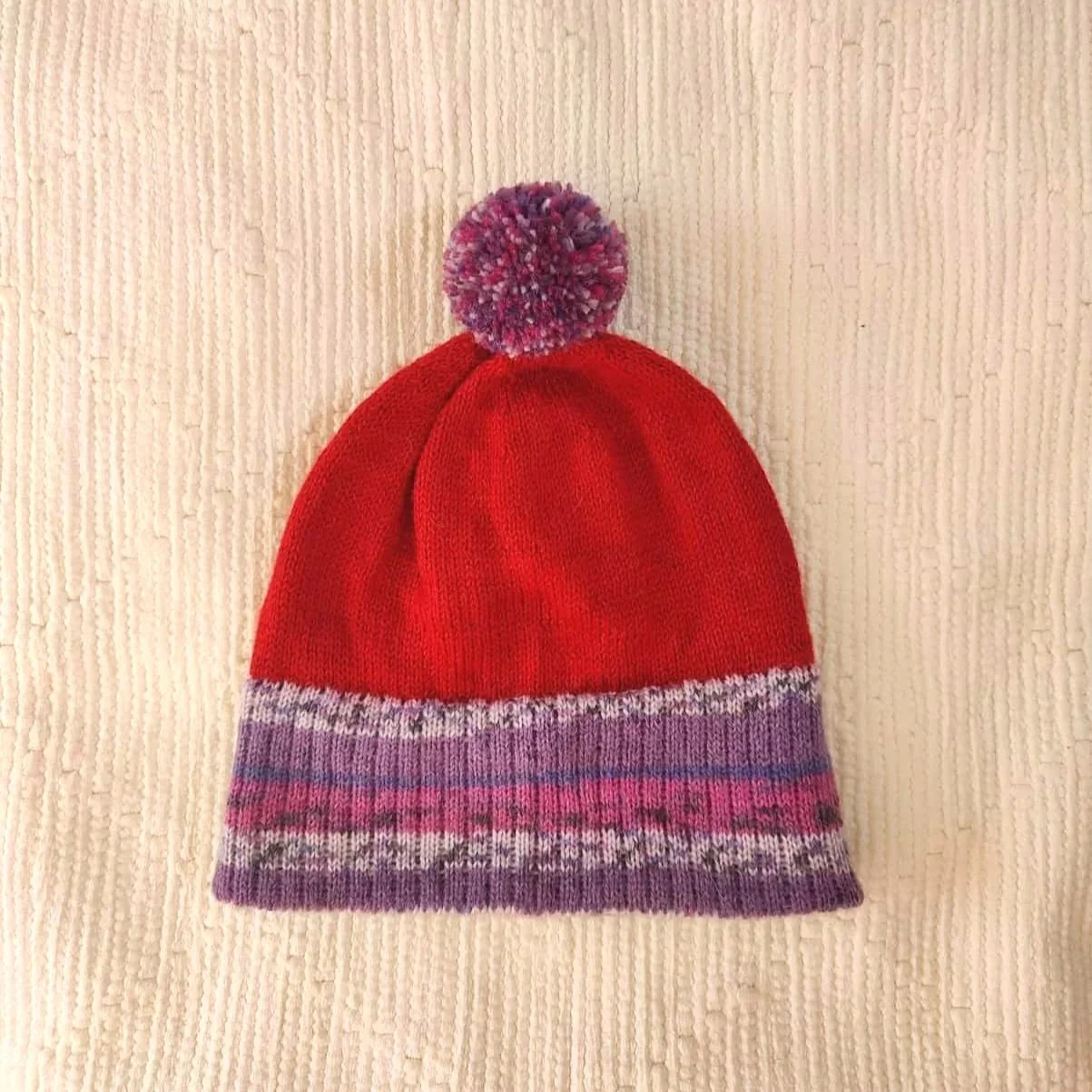 Bonnet artisanal tricoté en laine rouge avec pompon et revers violets à motifs pour enfant
