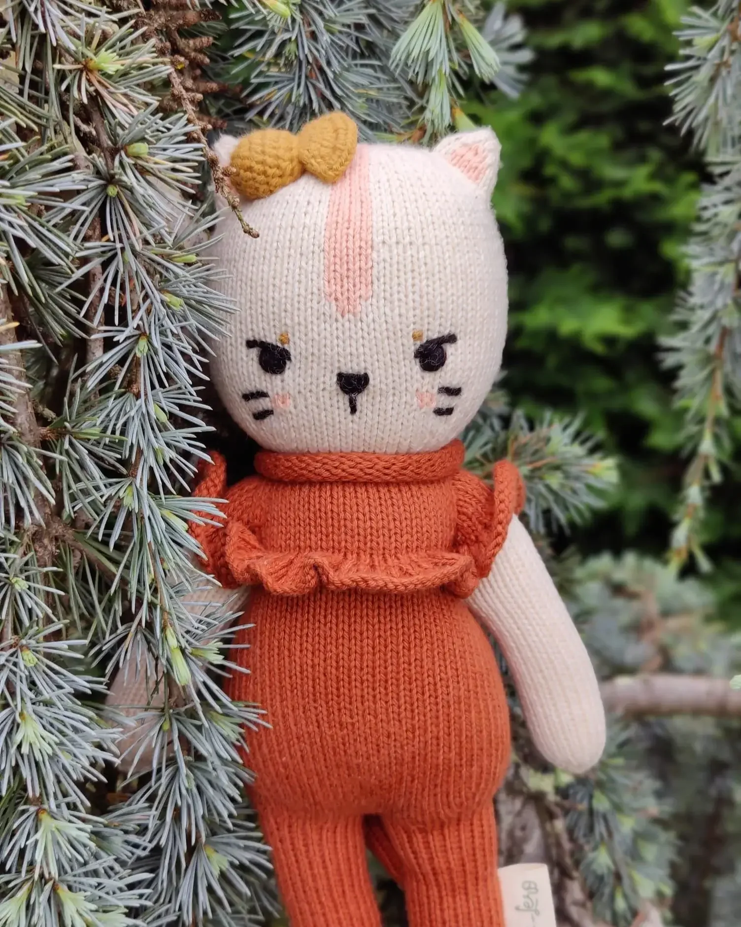 Le doudou chat Ima tricoté artisanalement à côté d'un sapin
