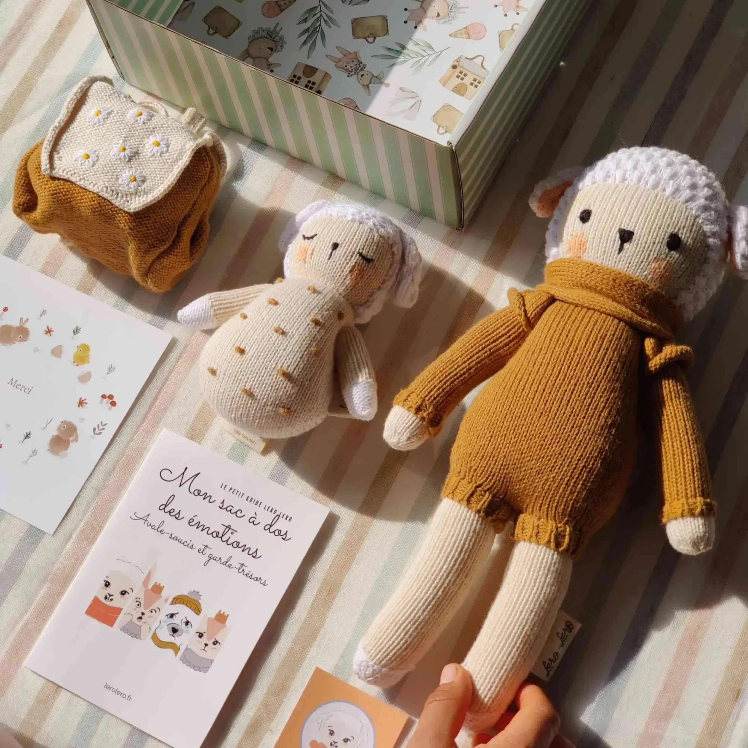 Détail sur la composition du coffret naissance Nino Caramel le Mouton : peluche Nino Caramel, sac à dos des émotions à broderies fleurs et hochet. Tricotés en coton bio.