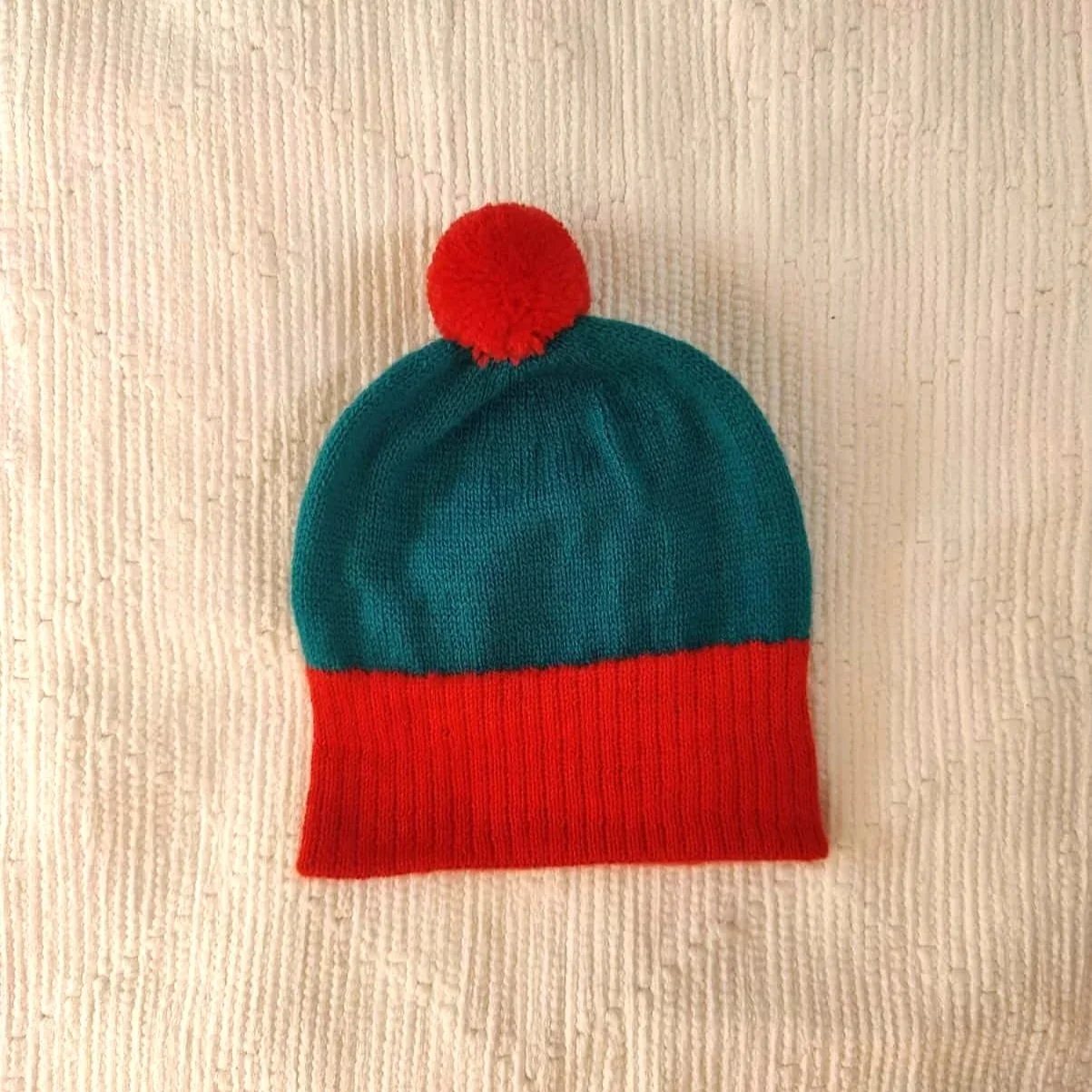 Bonnet artisanal tricoté en laine vert avec pompon et revers rouges pour enfant