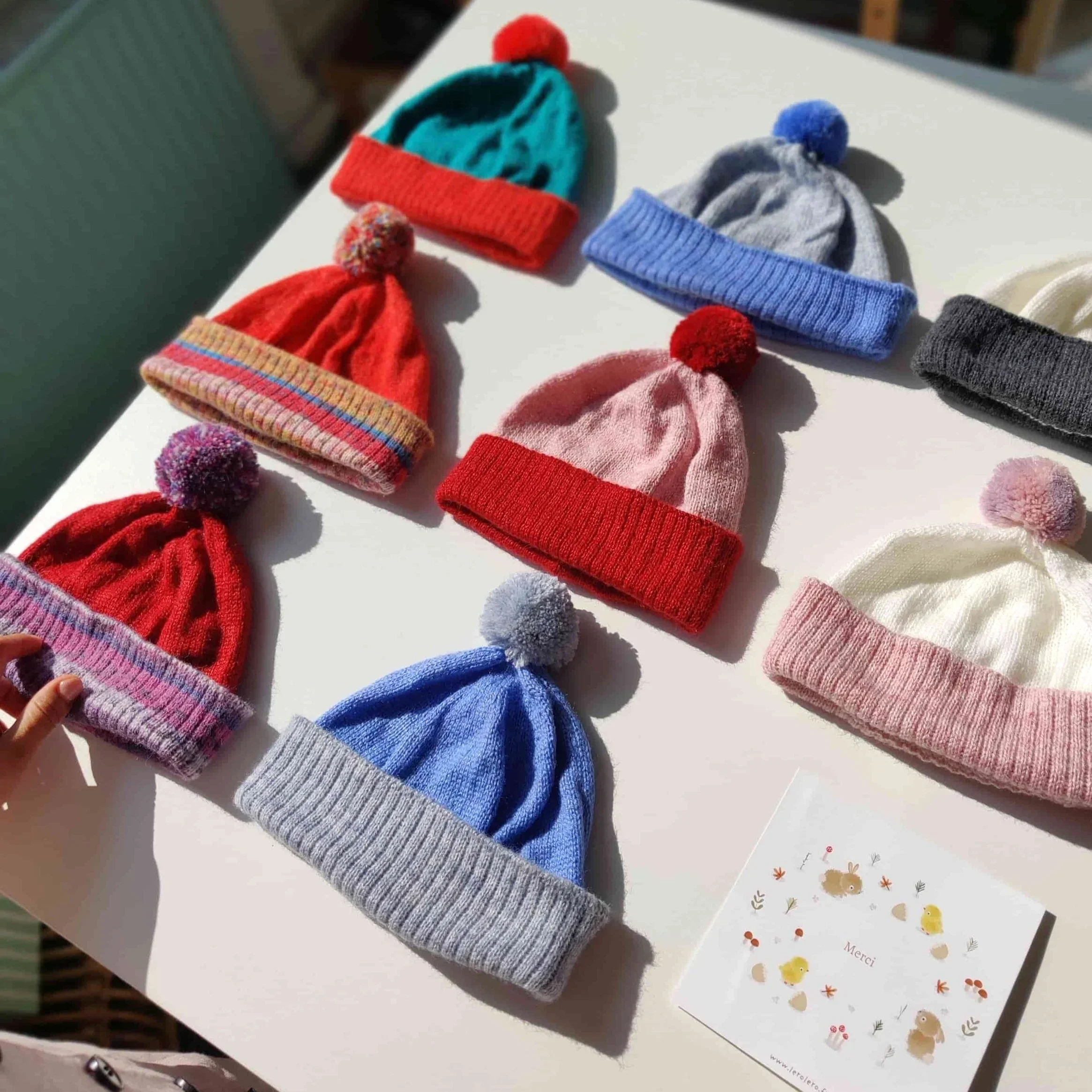 Plusieurs modèles de bonnets tricotés en laine à pompon pour enfant exposés sur une table